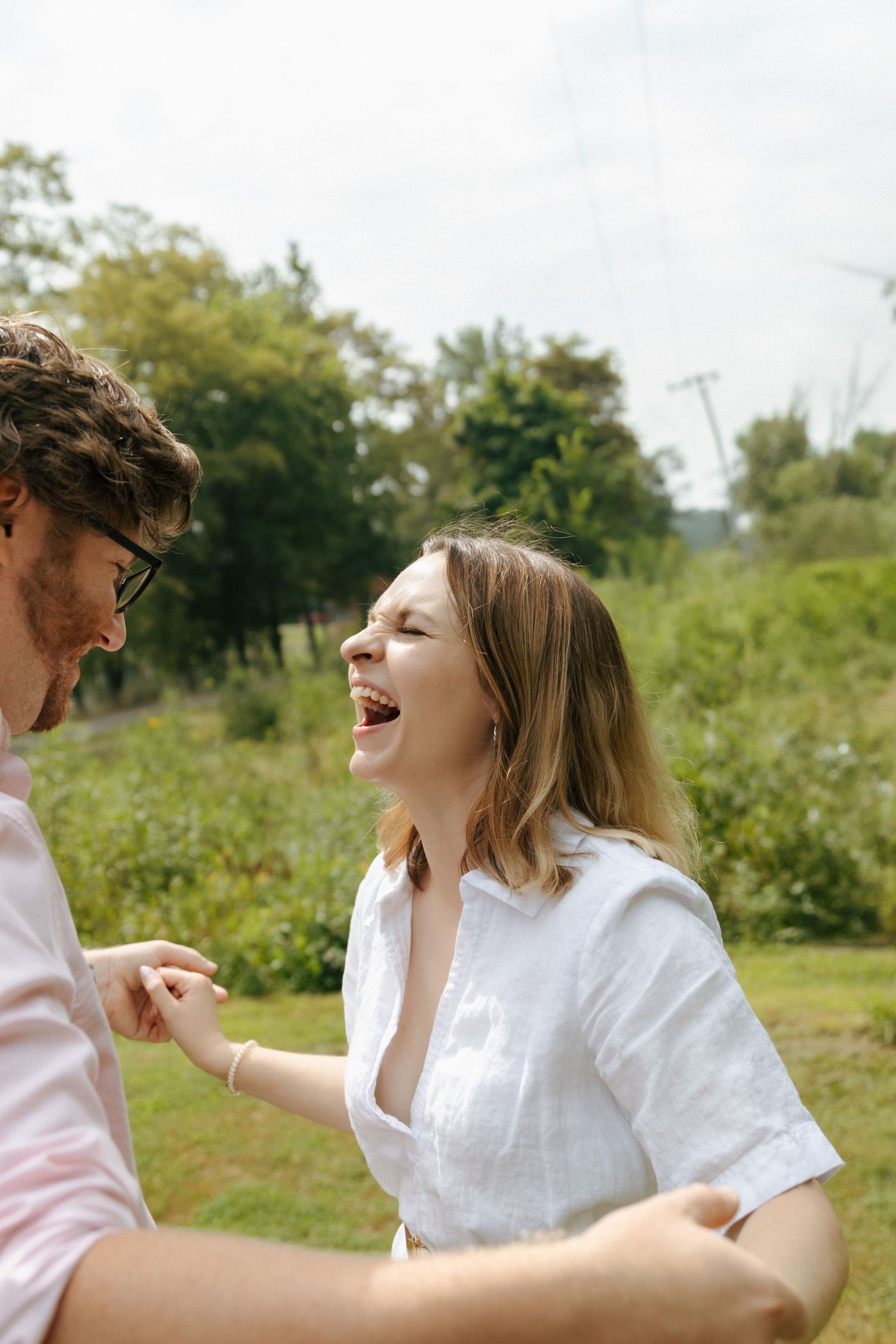 A joyful candid moment captured outdoors with two people laughing together on a sunny summer day.