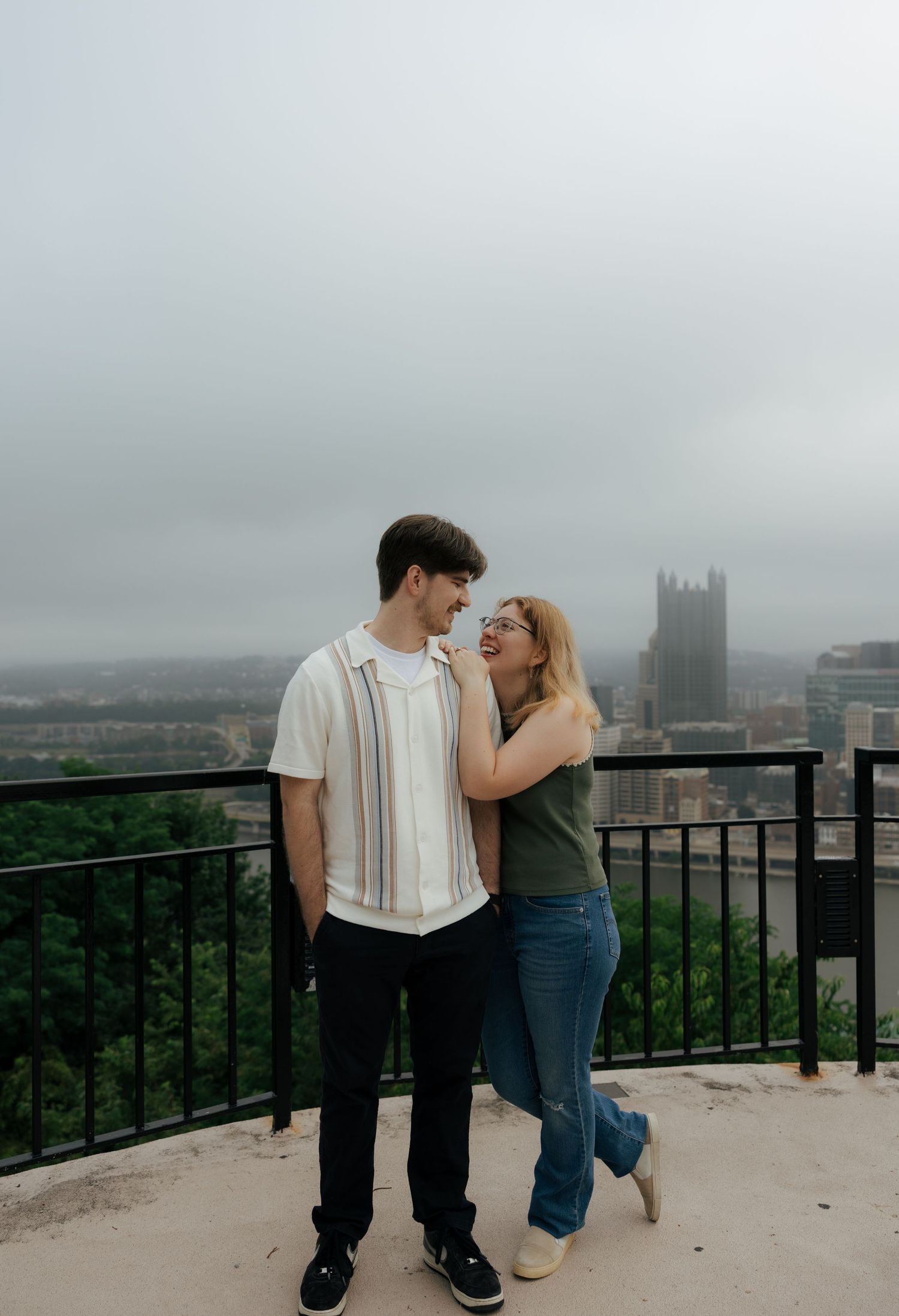 Romantic couple embracing and smiling at each other with a city skyline in the background.