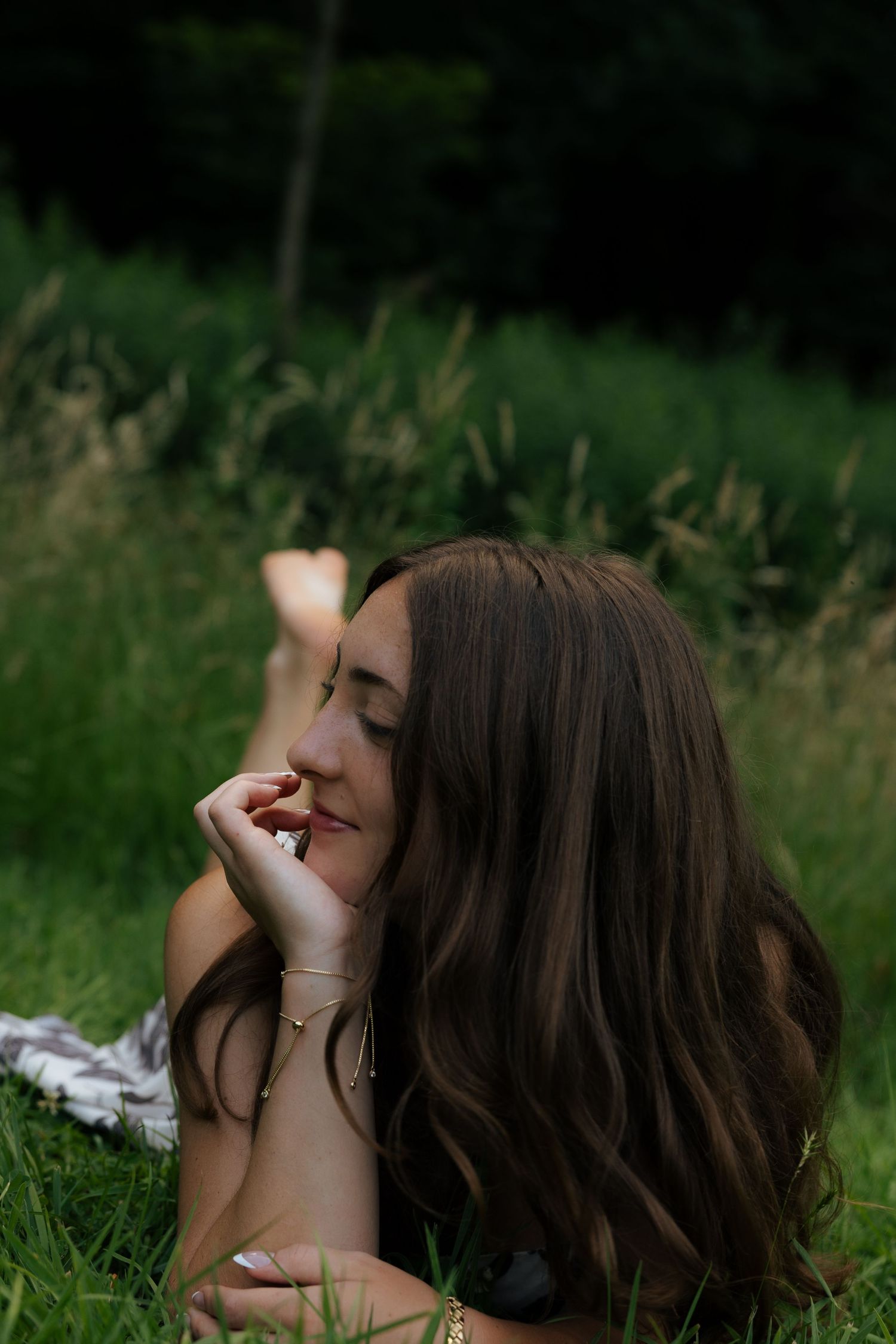Young woman lying in grass, smiling softly with eyes closed.