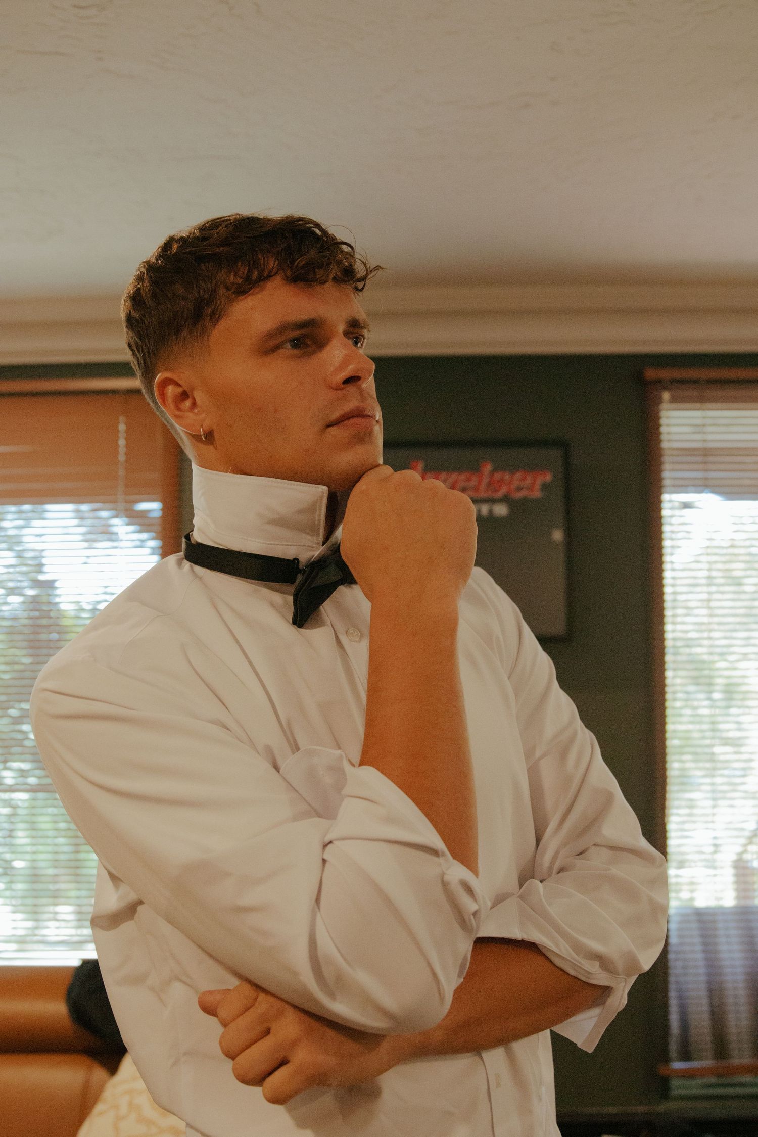 Groom in white dress shirt adjusting black bow tie while getting ready for wedding ceremony.