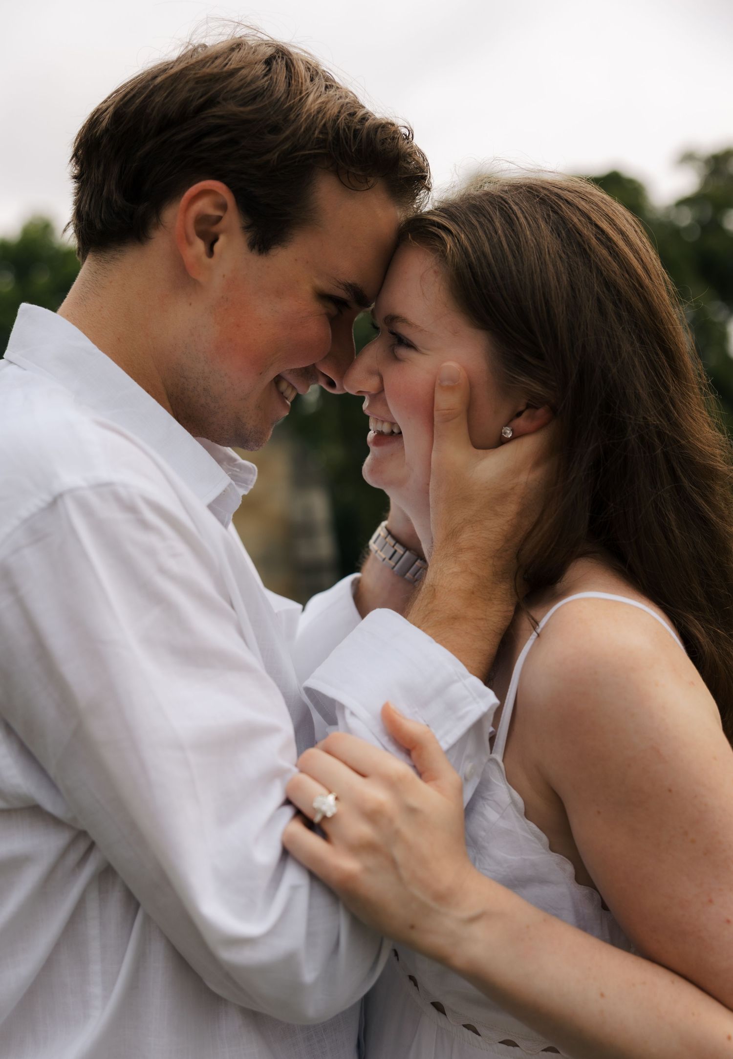 Happy engaged couple touching foreheads and smiling, woman showing diamond engagement ring.