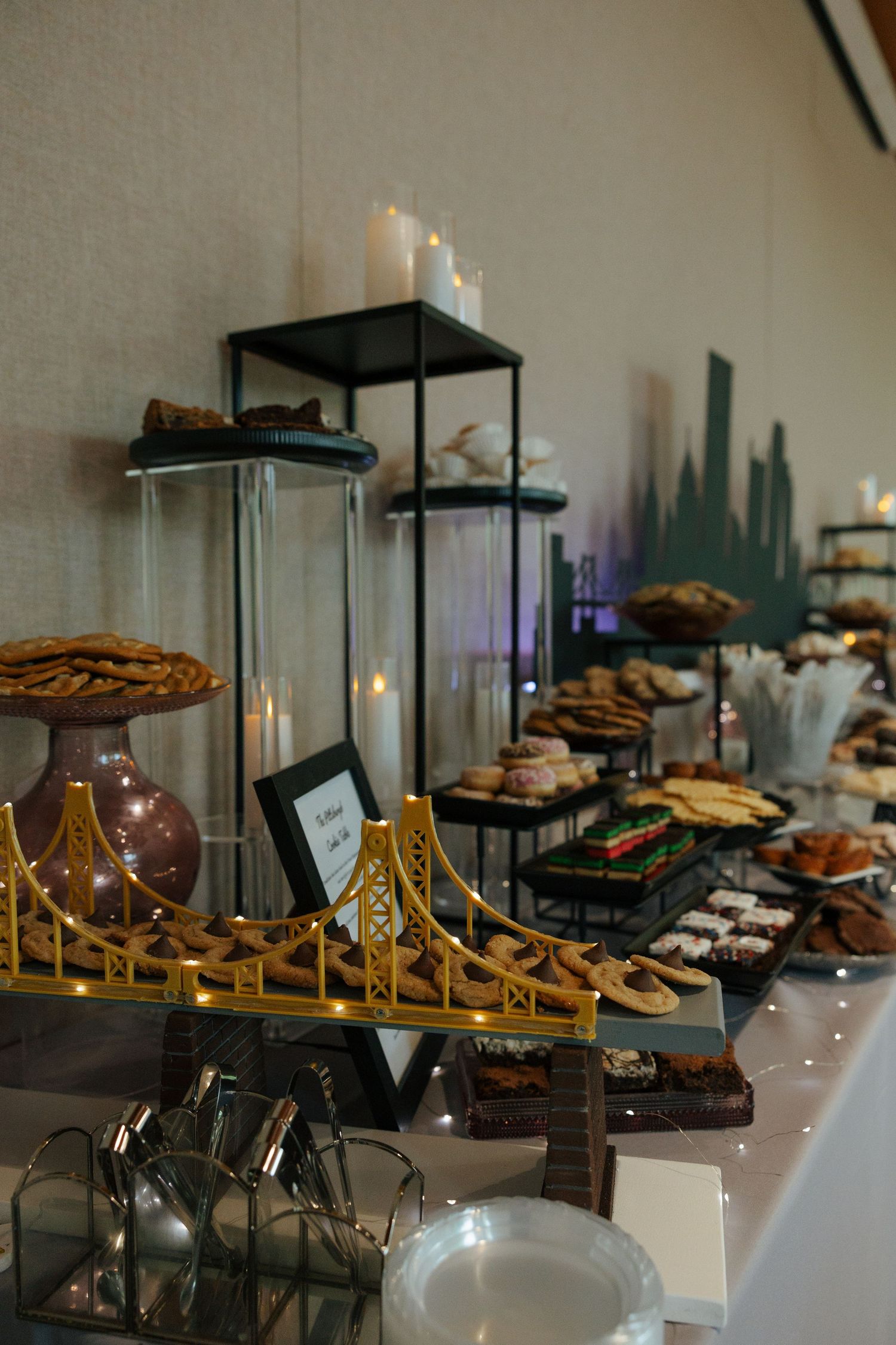 Wedding dessert table with golden bridge centerpiece, tiered treats, cookies, and candles on display.