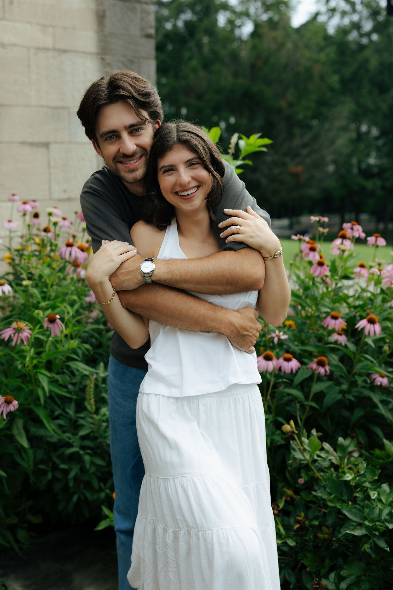A happy couple hugs in a garden full of pink coneflowers, the man wrapping his arms around the woman in white.