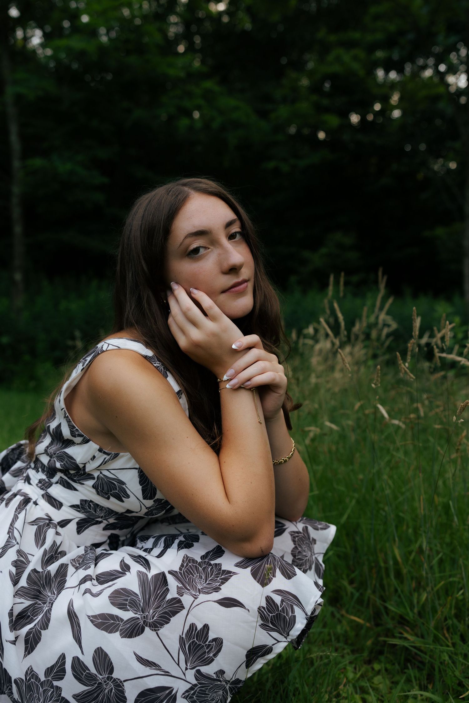Young woman in floral dress sitting thoughtfully in a green field.