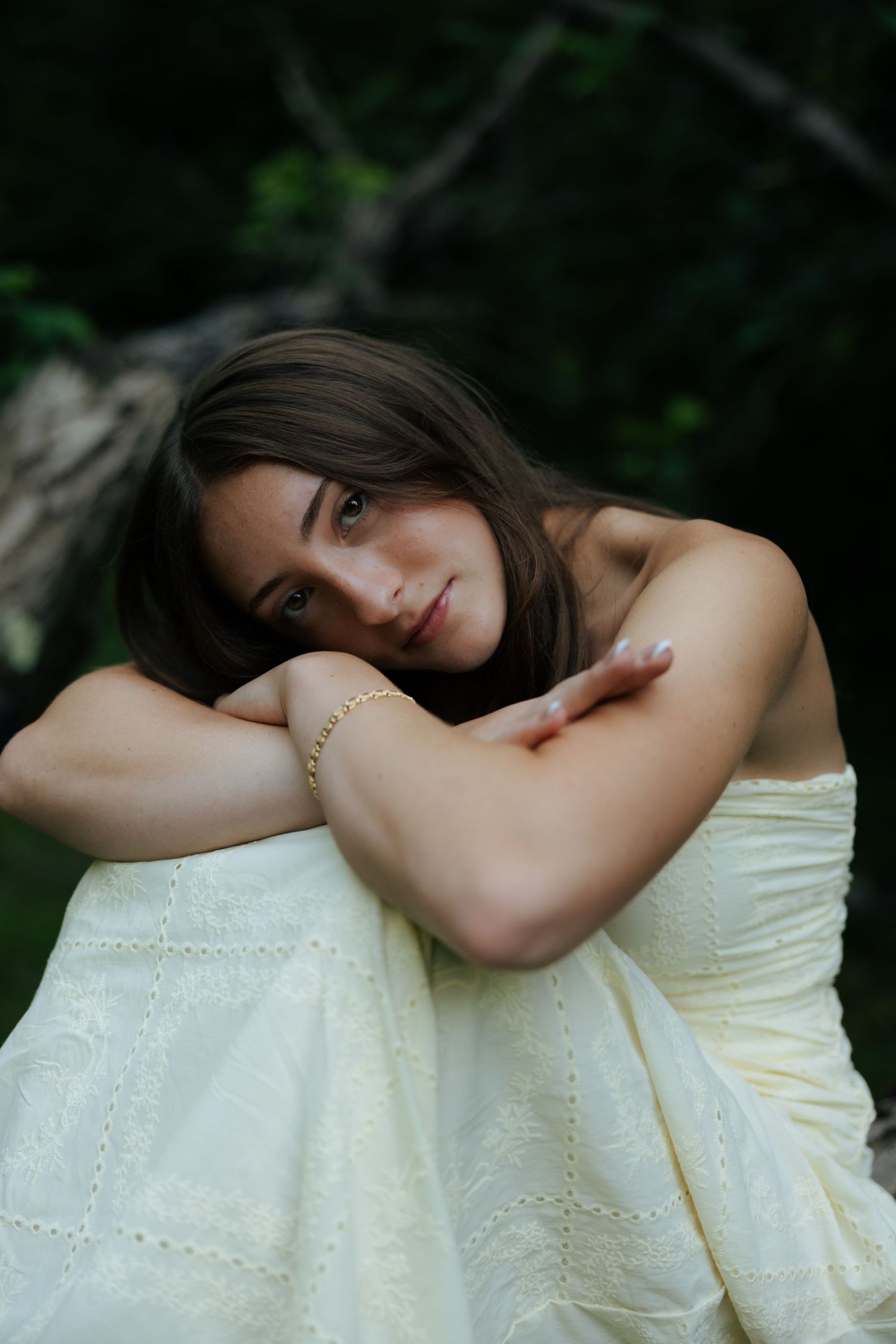 Young woman in yellow dress resting chin on arms outdoors.