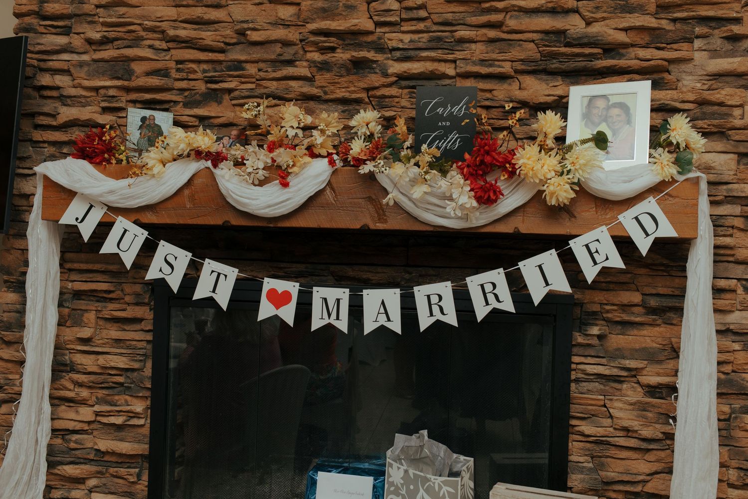 Rustic wedding venue fireplace mantel decorated with Just Married banner, flowers, and white fabric garland.
