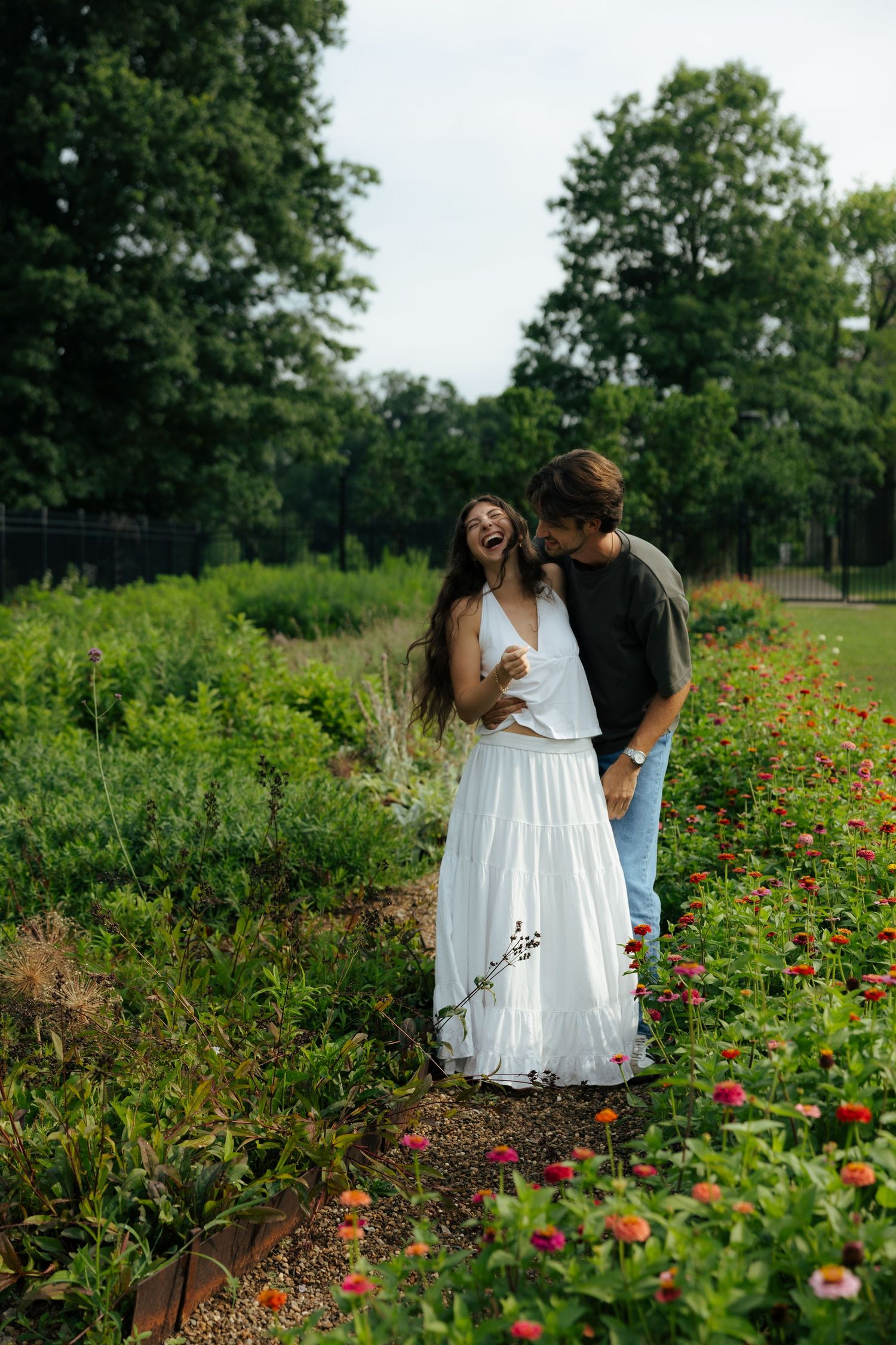 A joyful couple laughs together while walking along a garden path lined with colorful blooming flowers.