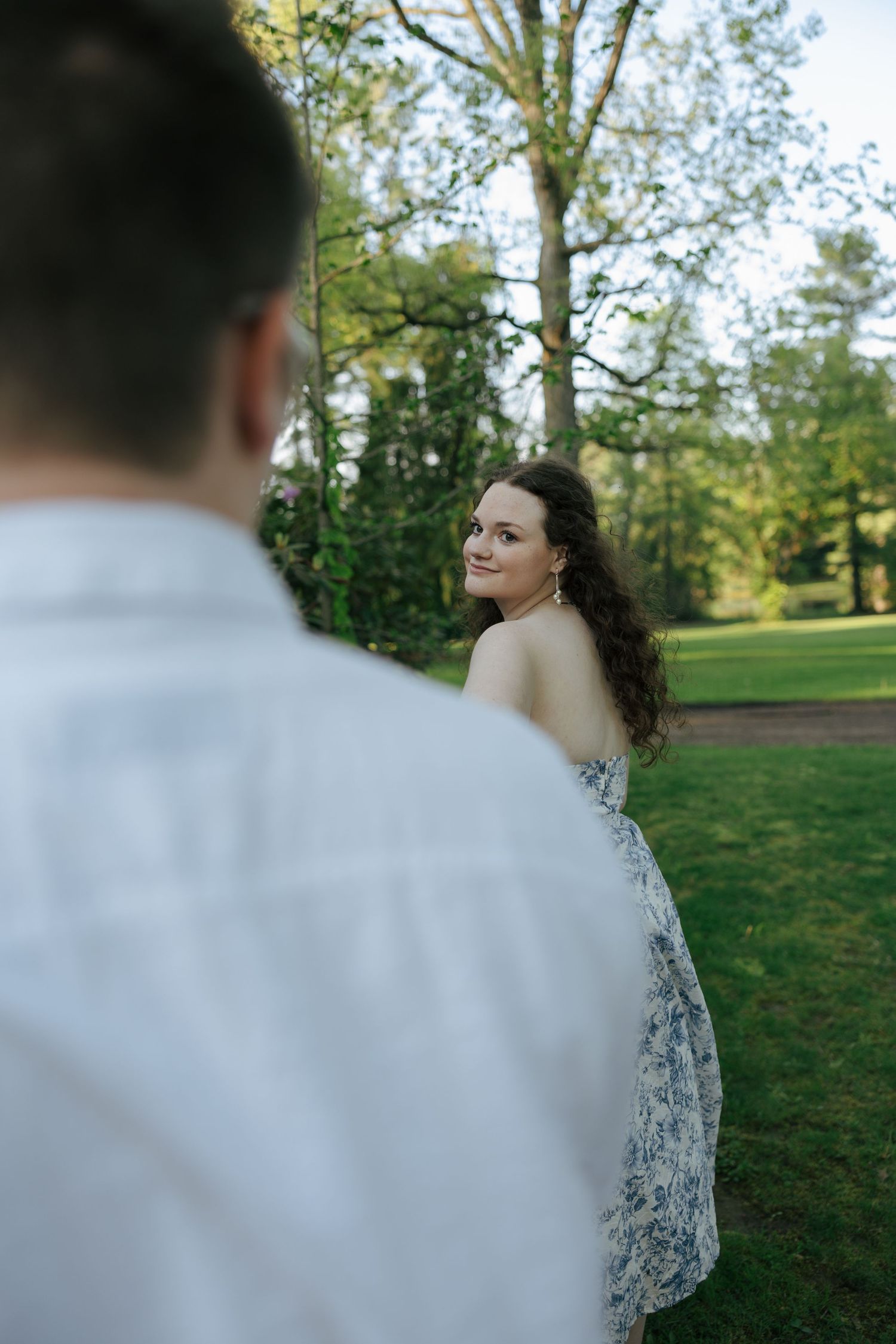 Woman in floral dress glancing back with a smile at her partner in a green park.