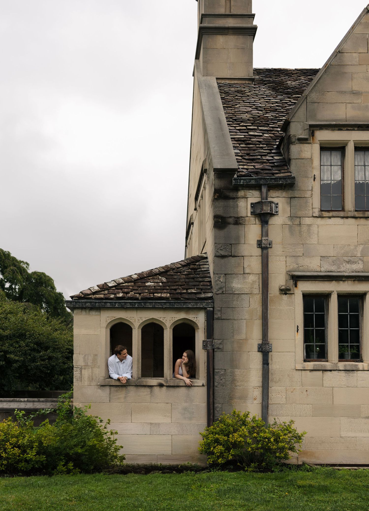Couple sitting together in an arched window alcove of a historic stone manor, chatting intimately.