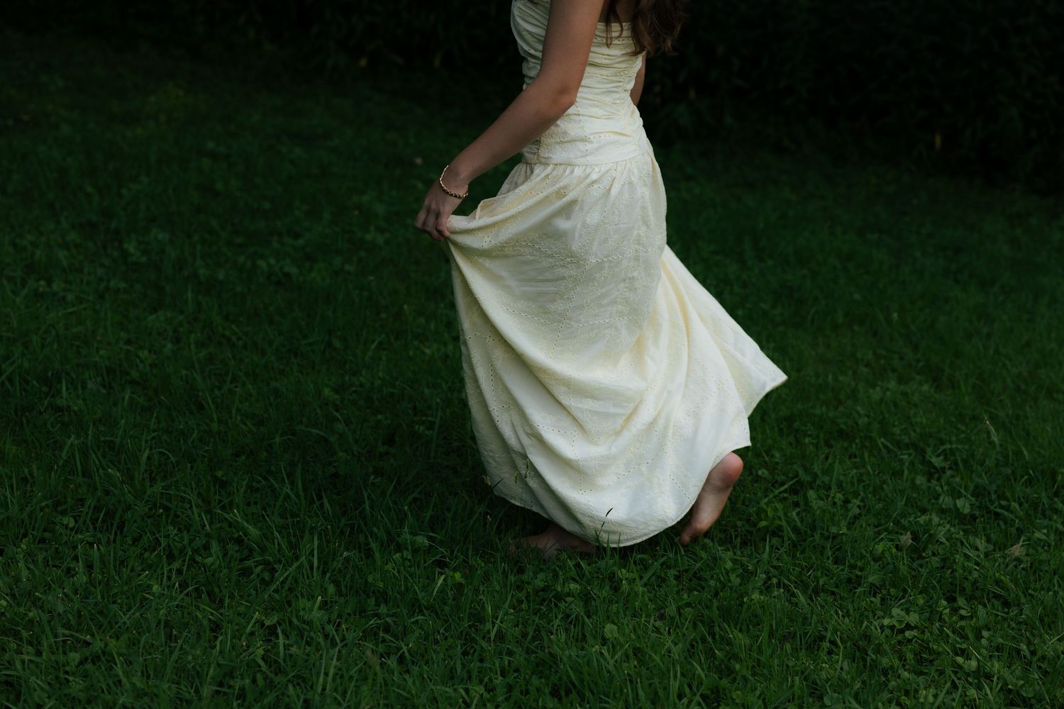 A woman in a flowing white wedding gown twirls gracefully on a lush green grass lawn.