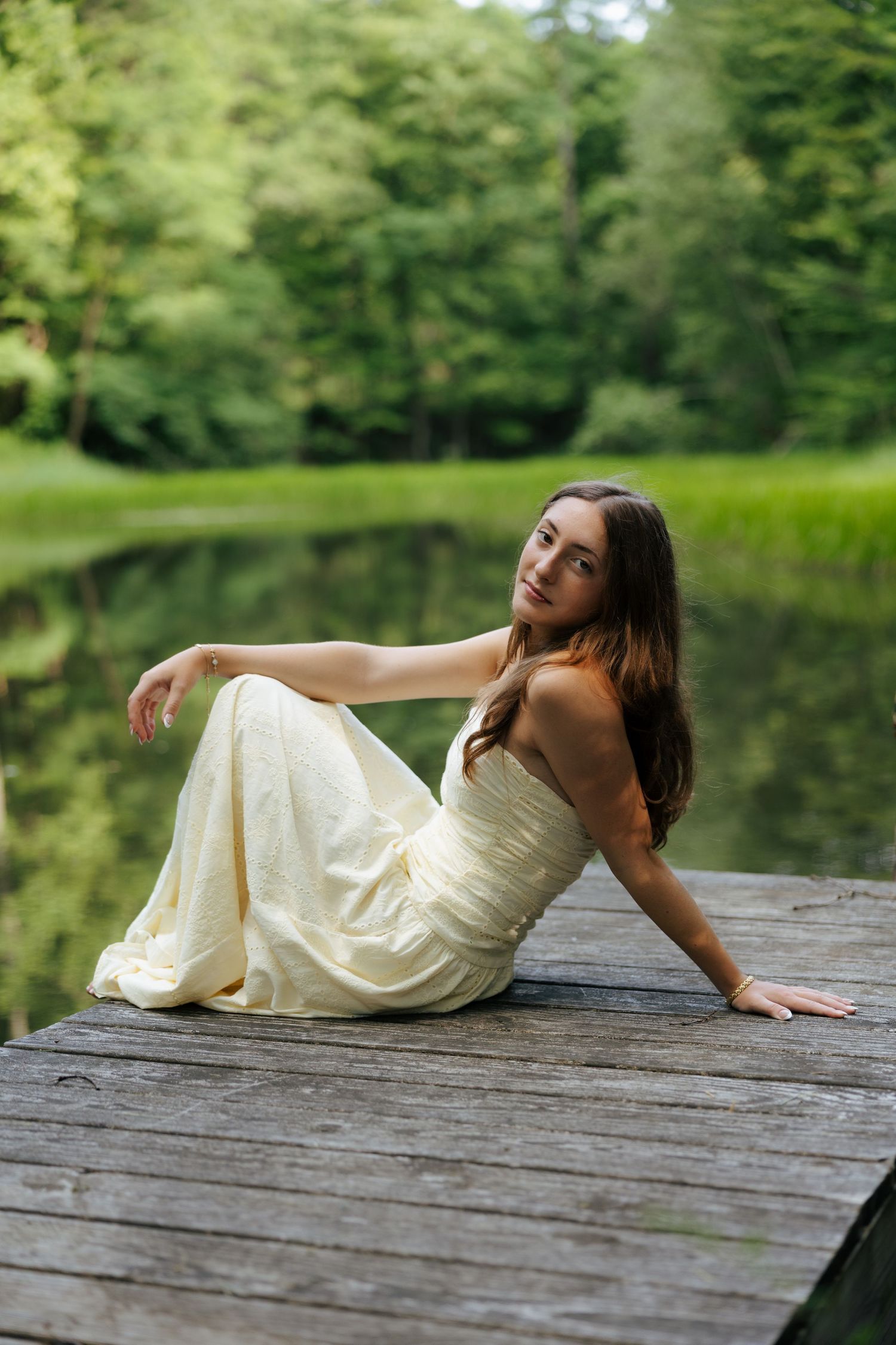 Young woman in white dress sitting gracefully on wooden lakeside dock.