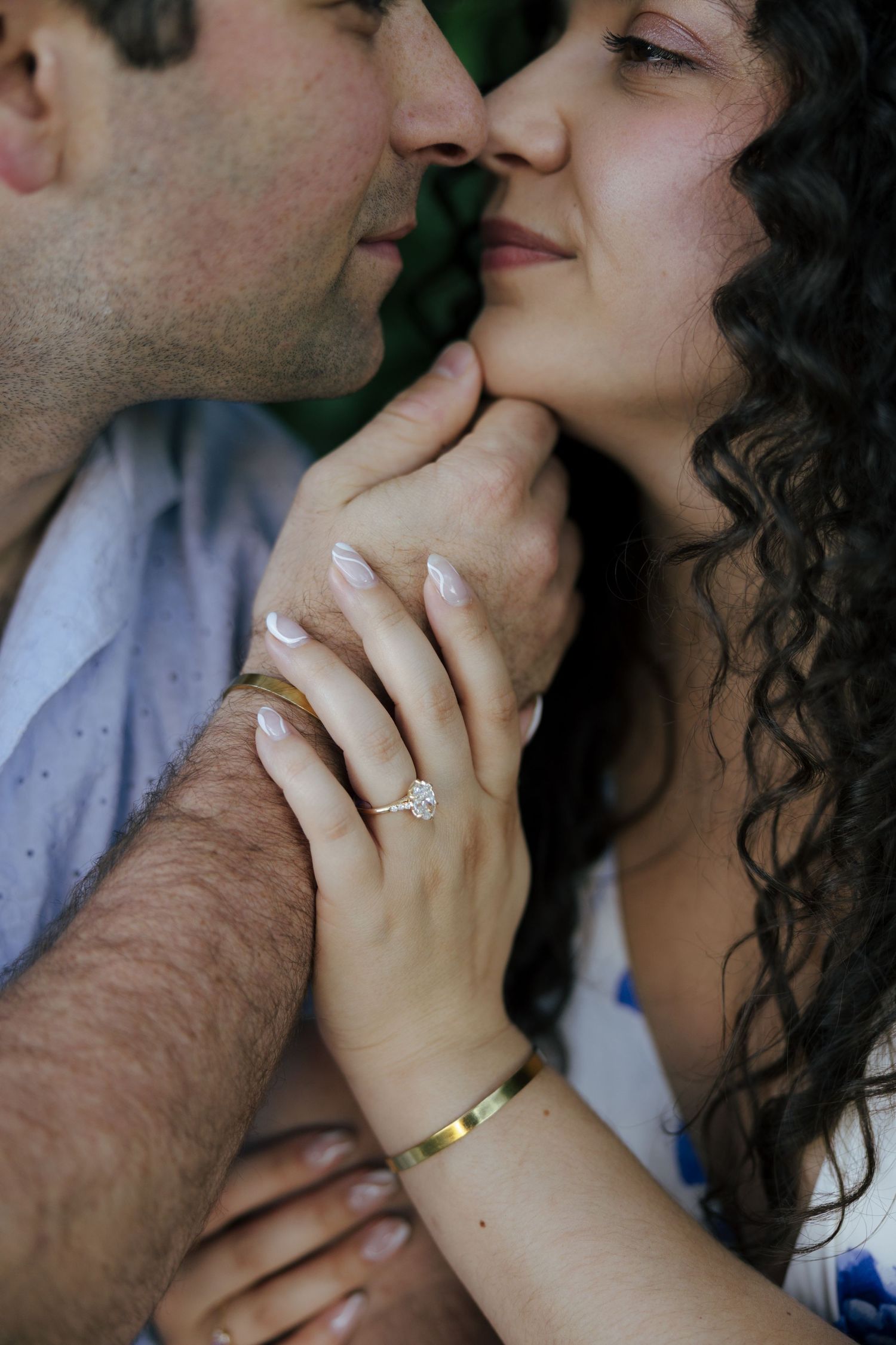Close-up of engaged couple almost kissing, showcasing a diamond engagement ring and gold bracelet.