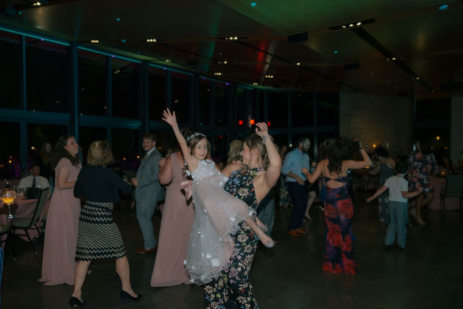 Guests dancing joyfully at an elegant wedding reception in a modern venue with colorful lighting.