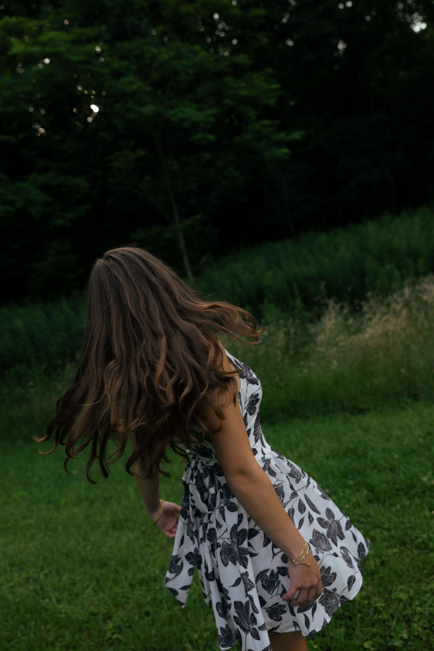 Woman in floral dress spinning in a green meadow, hair flowing.