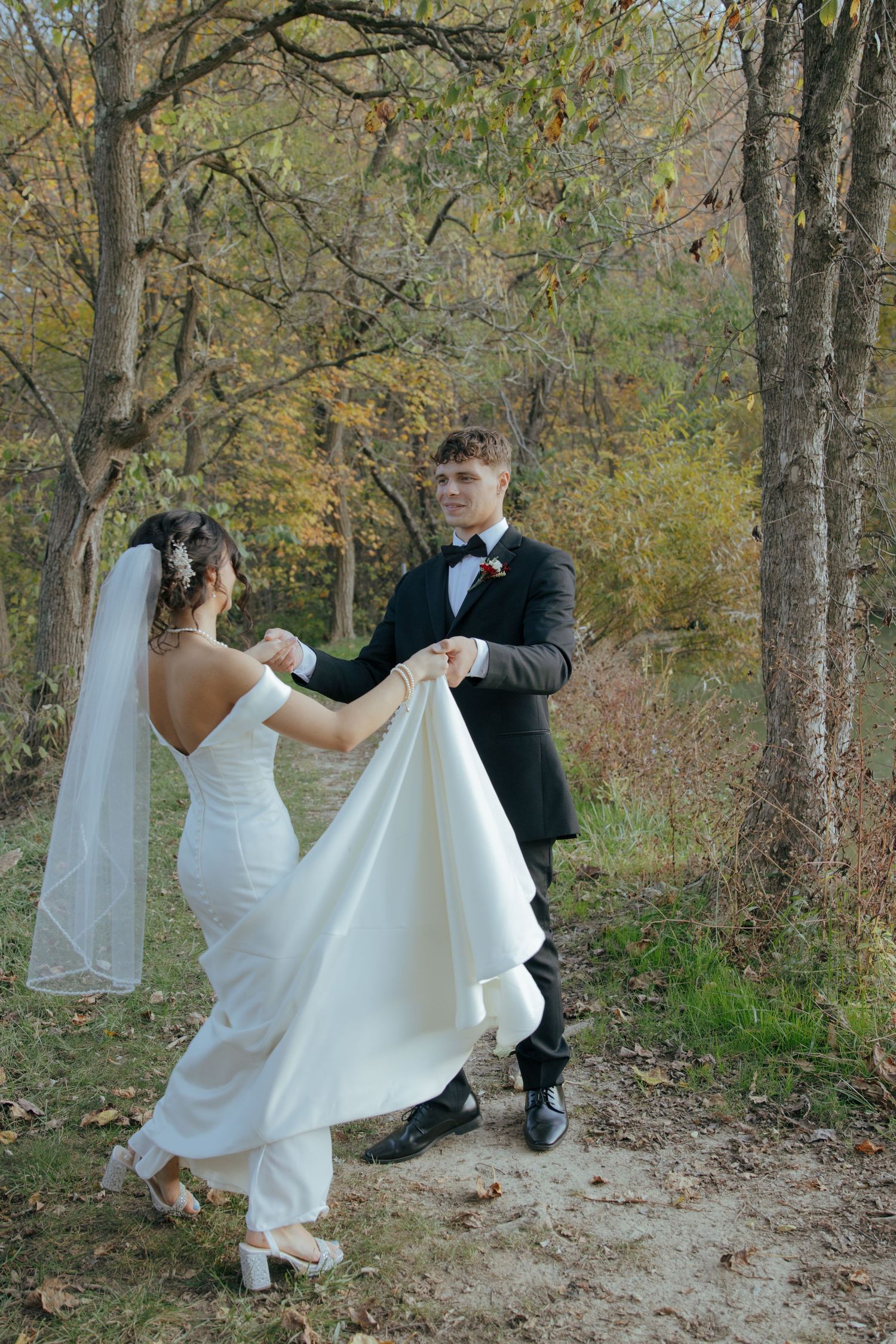 Bride and groom dancing playfully on a forest path surrounded by autumn foliage.