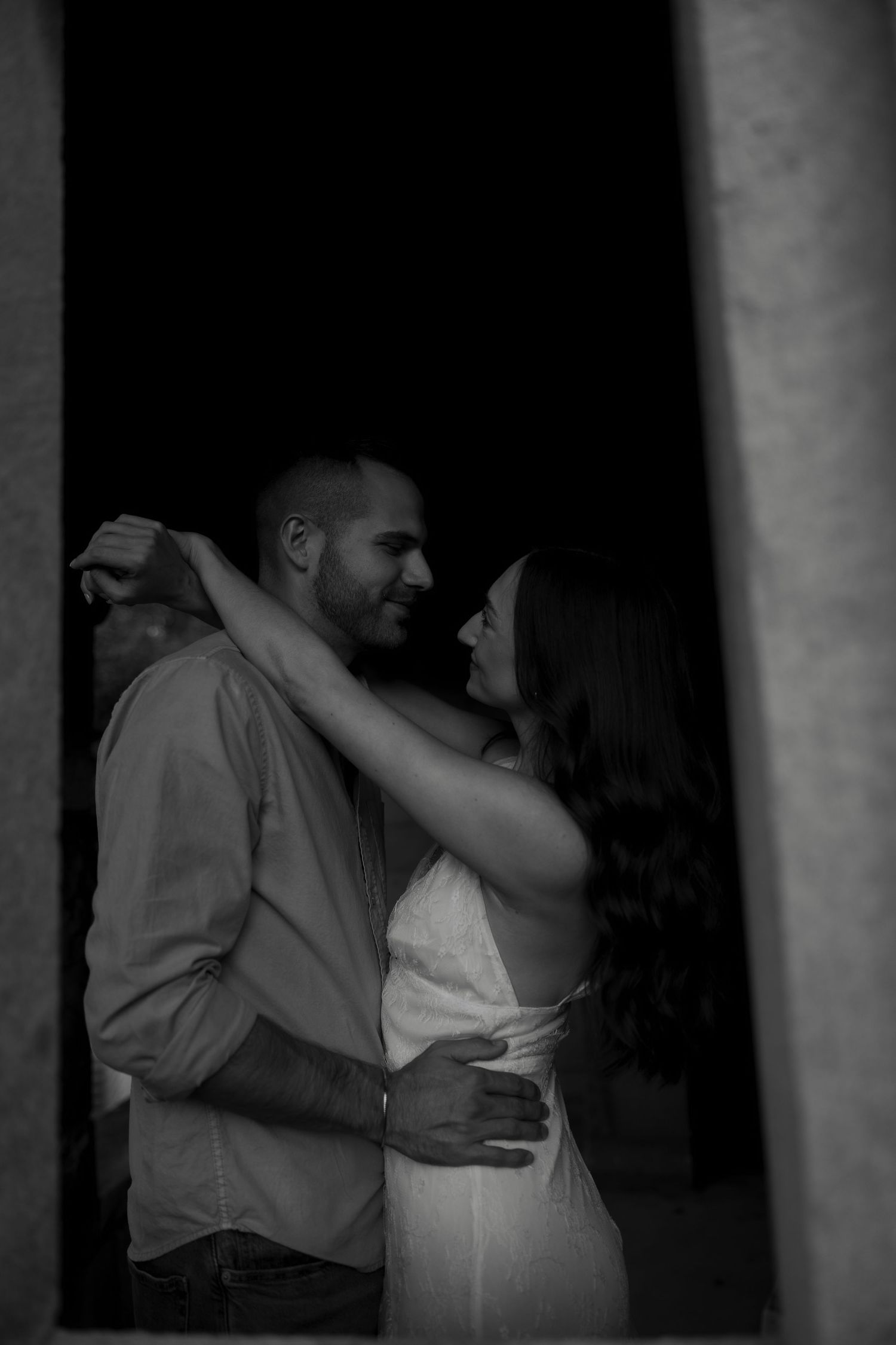 Black and white photo of a romantic couple embracing and smiling at each other in a doorway.