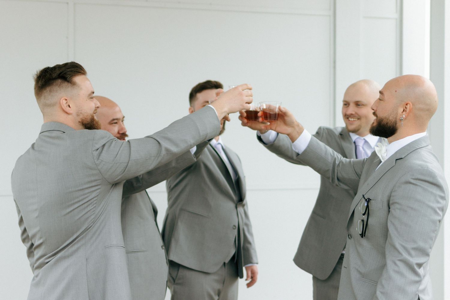 Groomsmen in matching gray suits toasting and celebrating together in a bright indoor setting.