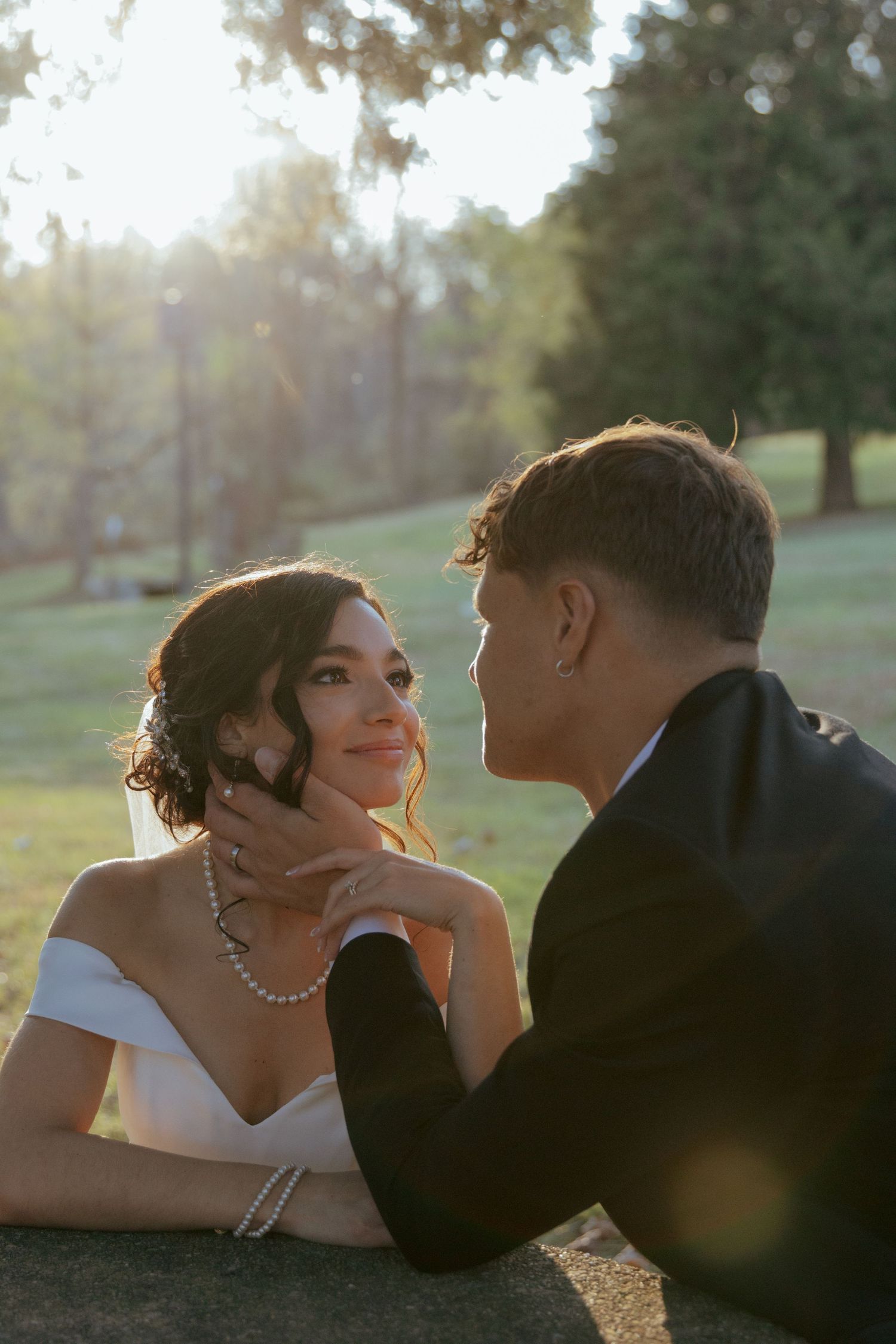 A couple in formal attire shares an intimate moment on the ground at sunset.