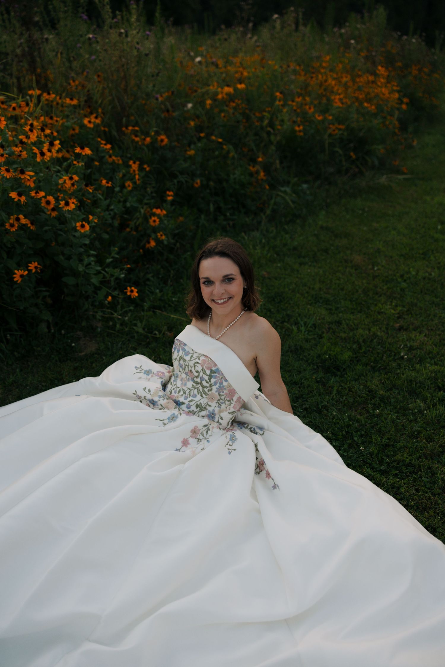 Bride sits in a voluminous white floral embroidered wedding gown surrounded by orange wildflowers.