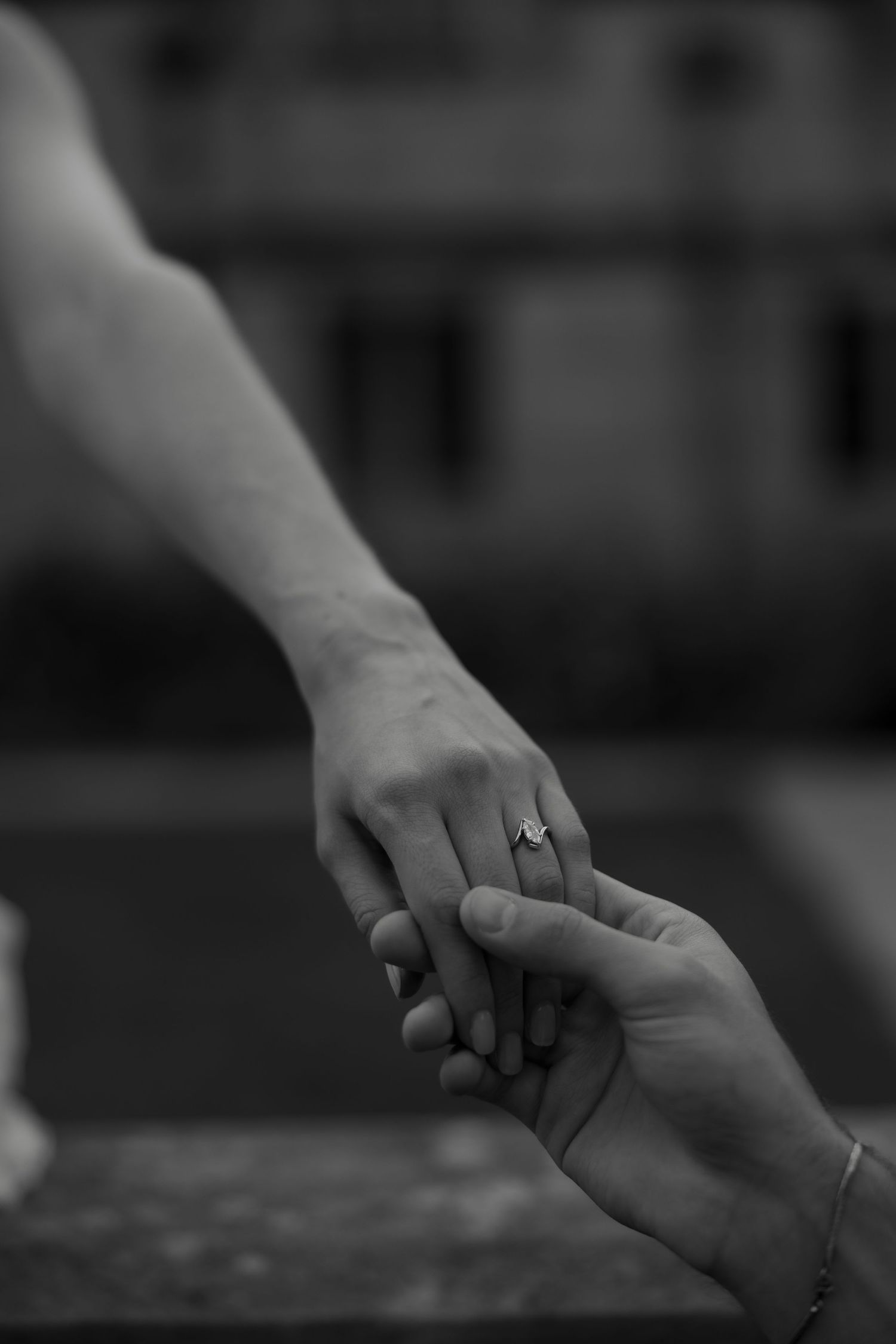 Black and white close-up of two hands touching, with a diamond engagement ring on the womans finger.
