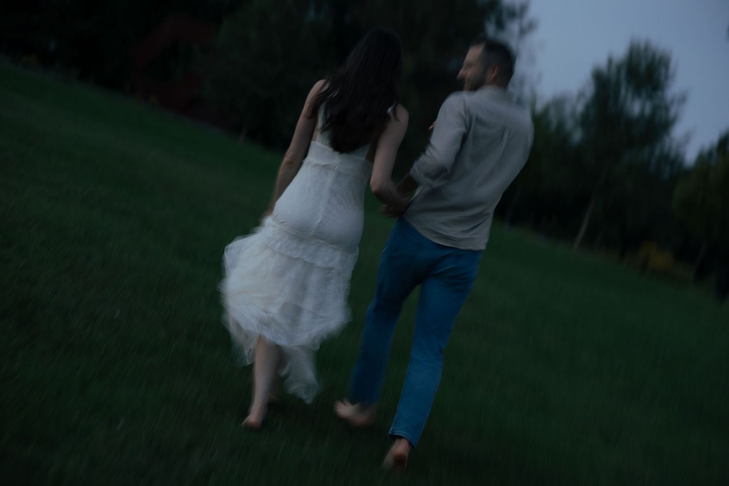 A blurred motion shot of a couple holding hands while walking across a green lawn at dusk.