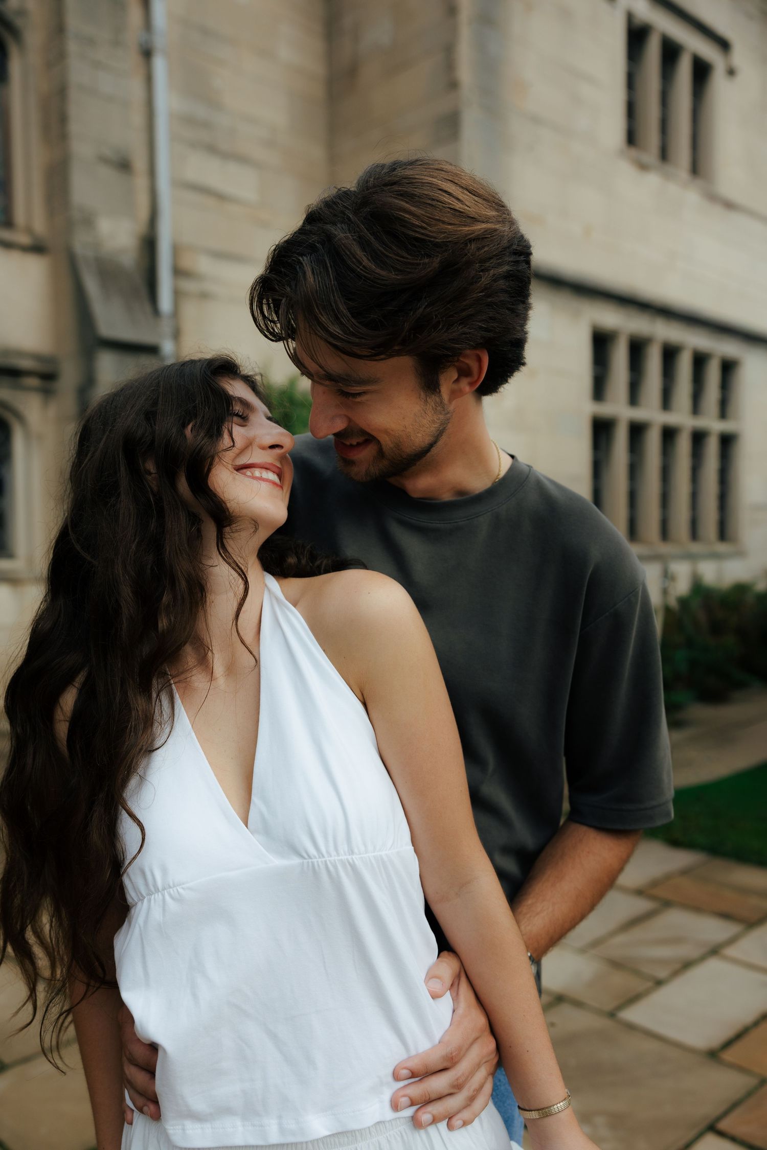 Happy couple embracing and smiling at each other outside a historic stone building.