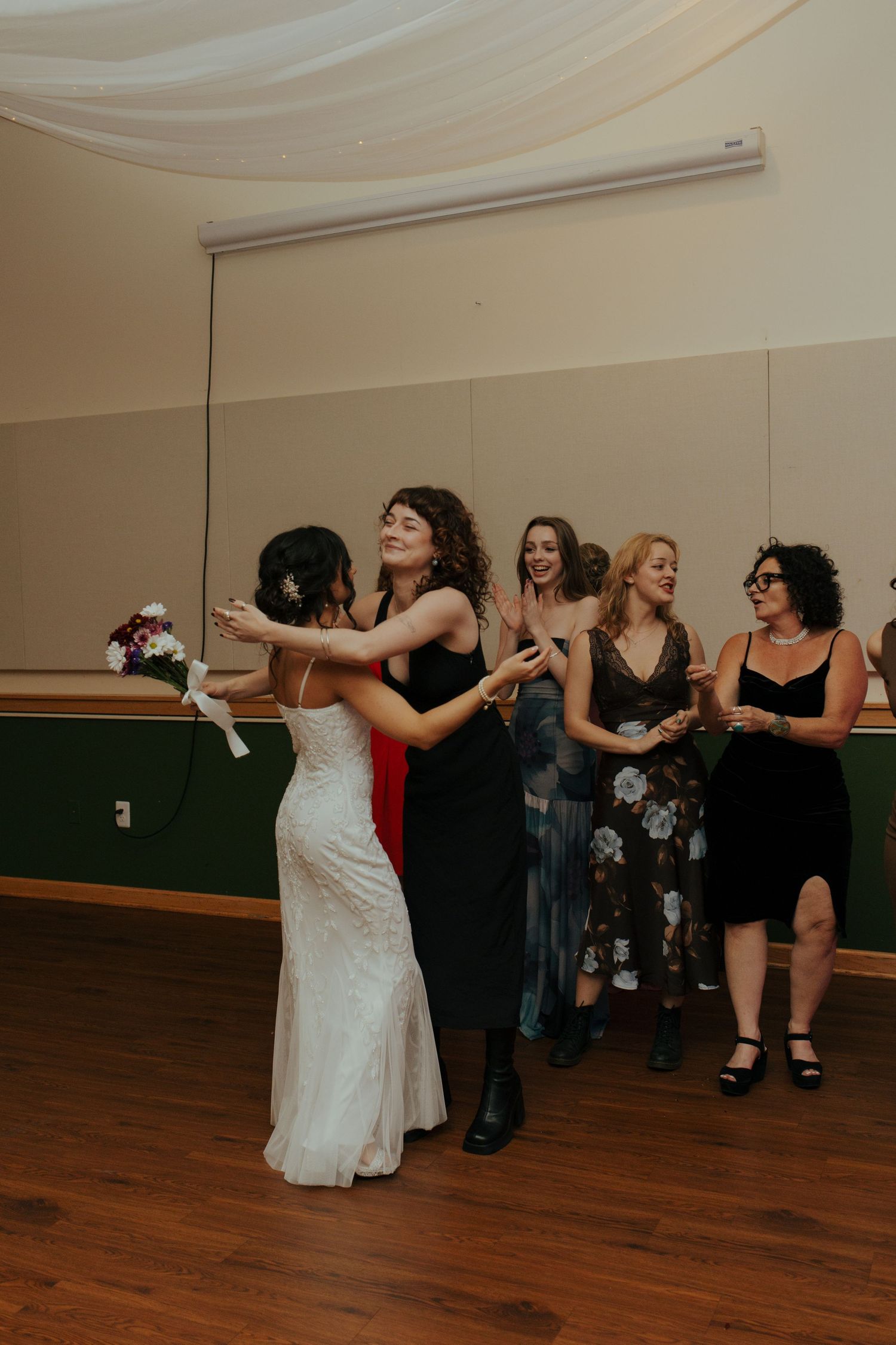 Bride prepares to toss her bouquet to excited female guests at the wedding reception.