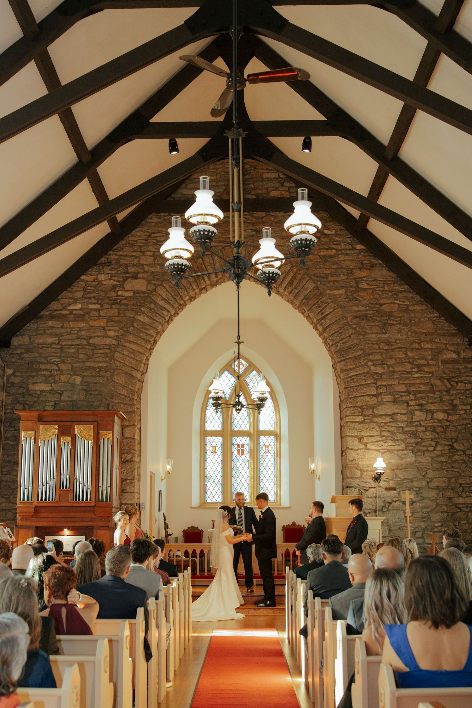 Wide angle view of elegant stone church interior with vaulted ceiling during wedding ceremony with seated guests.