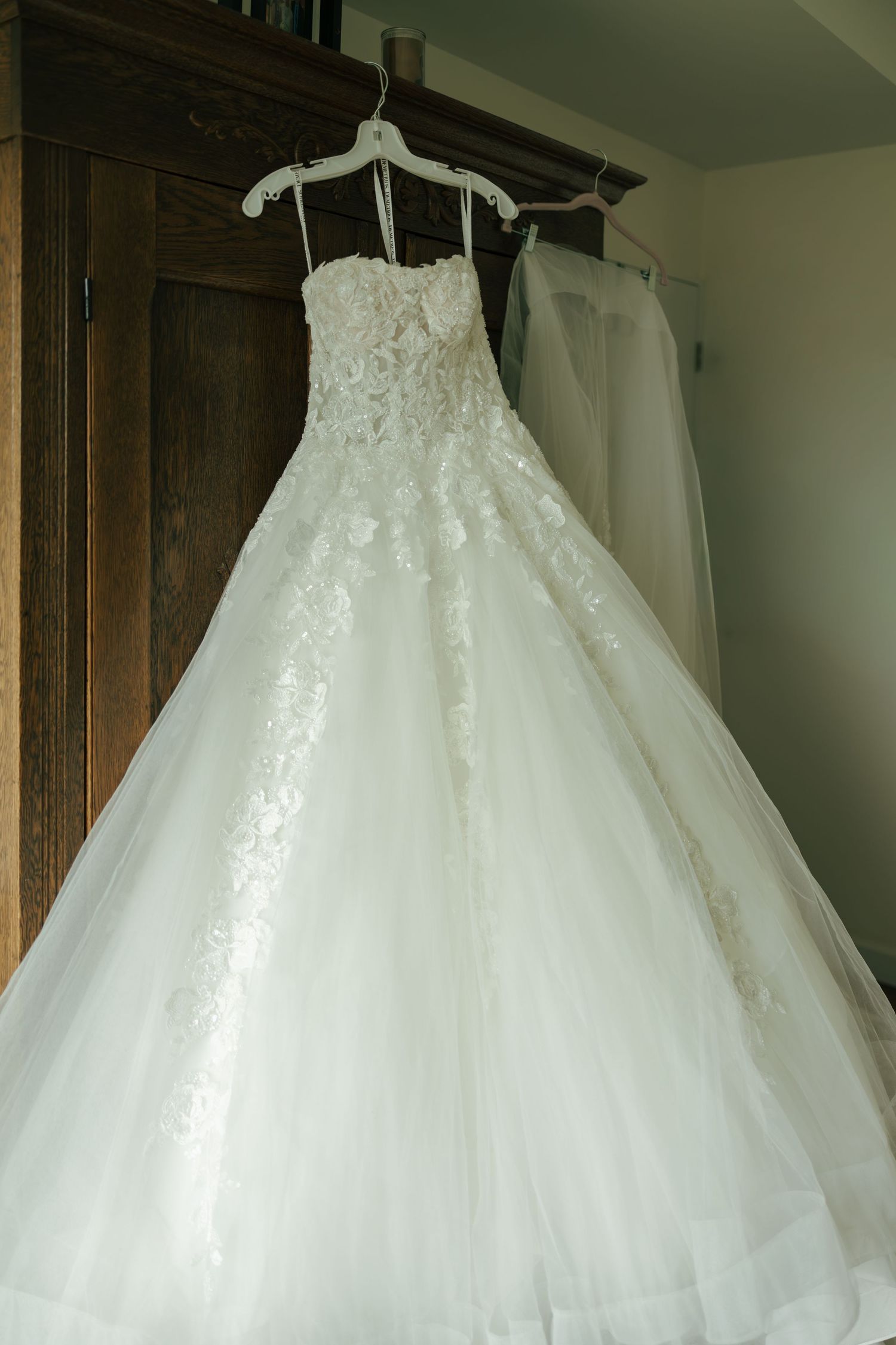 Elegant white ball gown wedding dress with lace bodice and full tulle skirt hanging on a wooden wardrobe.