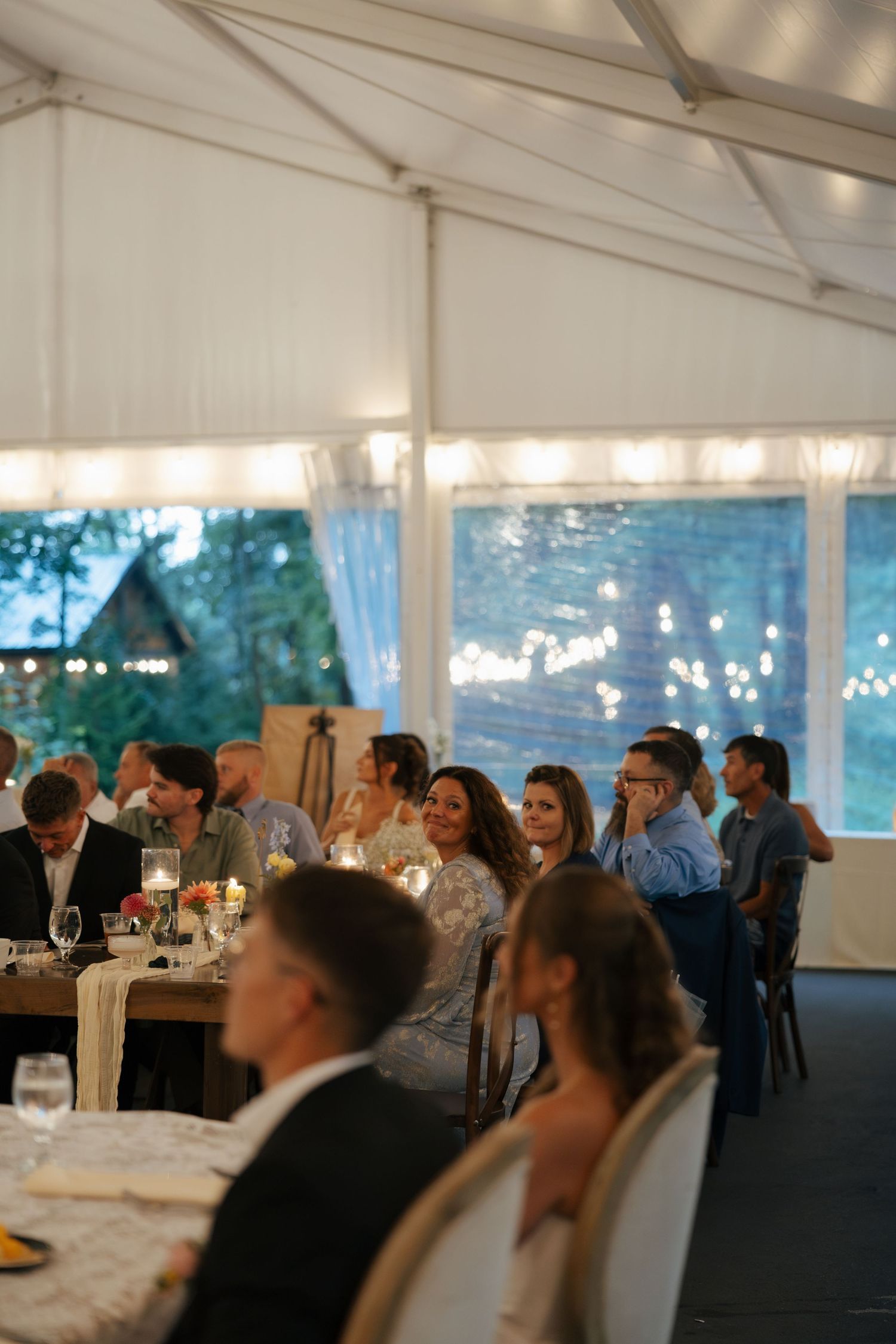 Guests seated at tables inside a elegant white tent venue during an evening wedding reception.