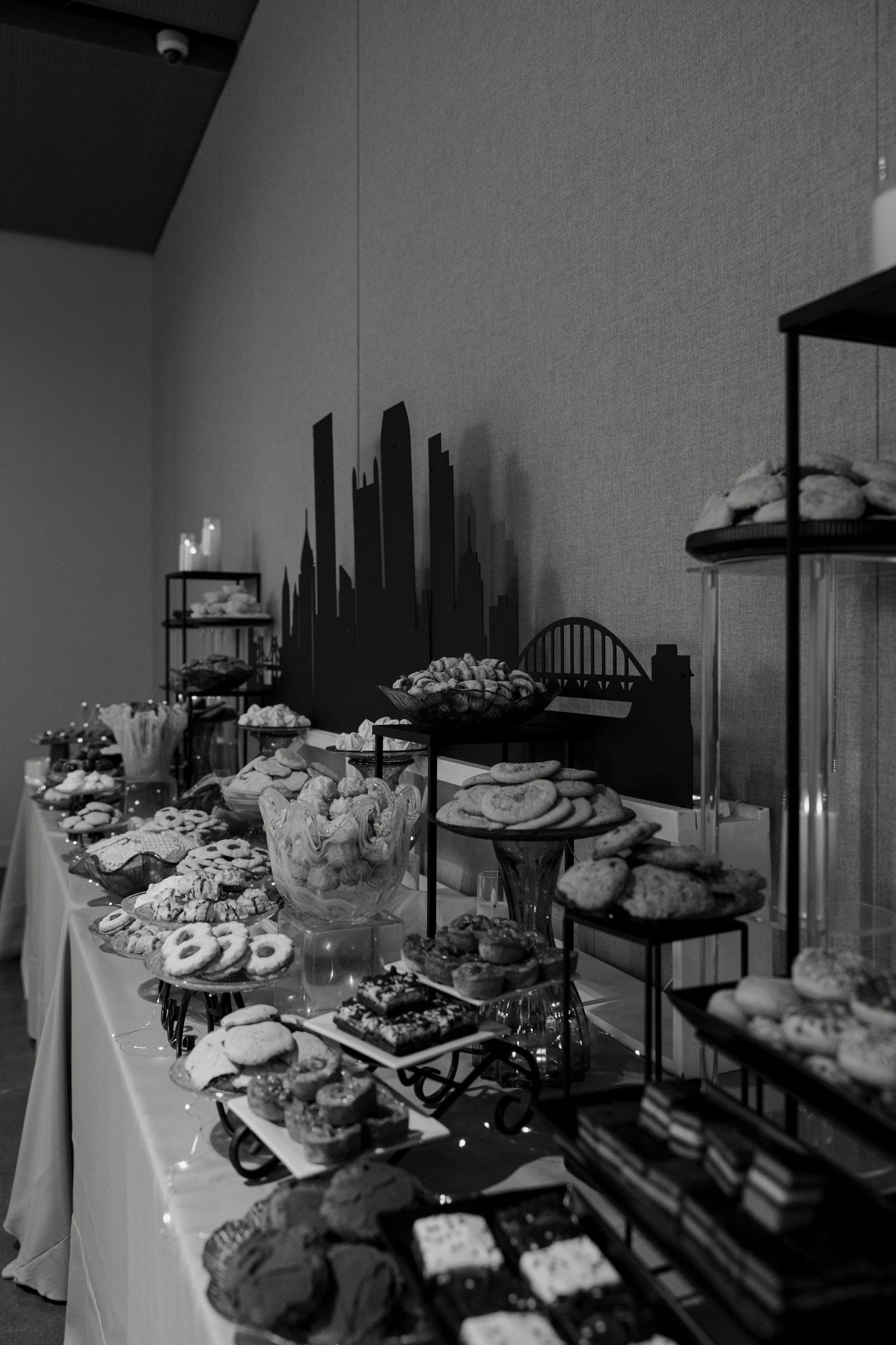 Black and white photo of an elegant dessert table filled with cookies, brownies, and sweets at a catered event.