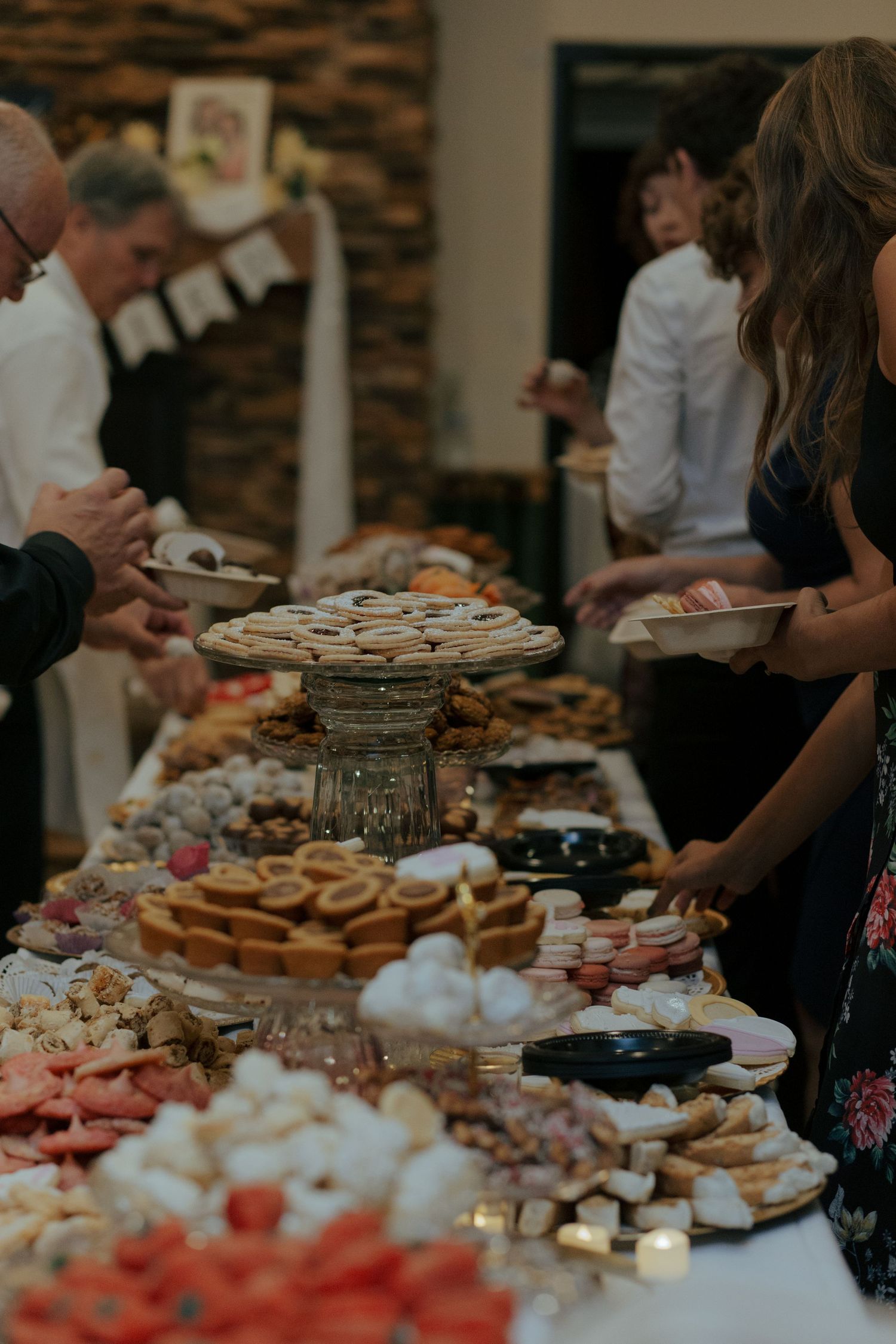 Guests enjoying elaborate wedding dessert table filled with colorful sweets, cookies, and macarons at reception.