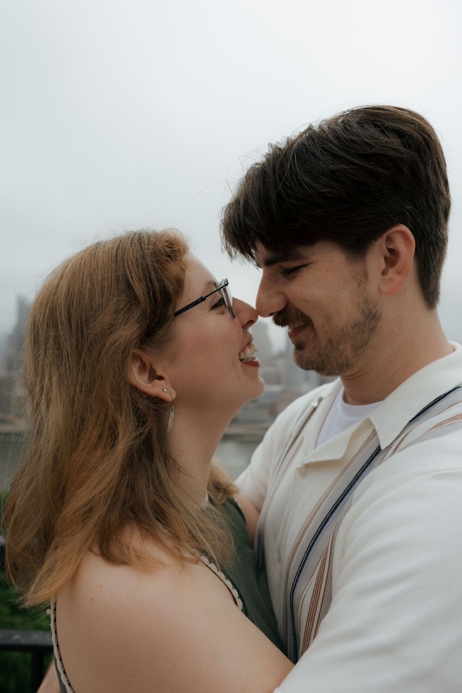 Close-up of a smiling couple leaning in for a kiss outdoors on an overcast day.