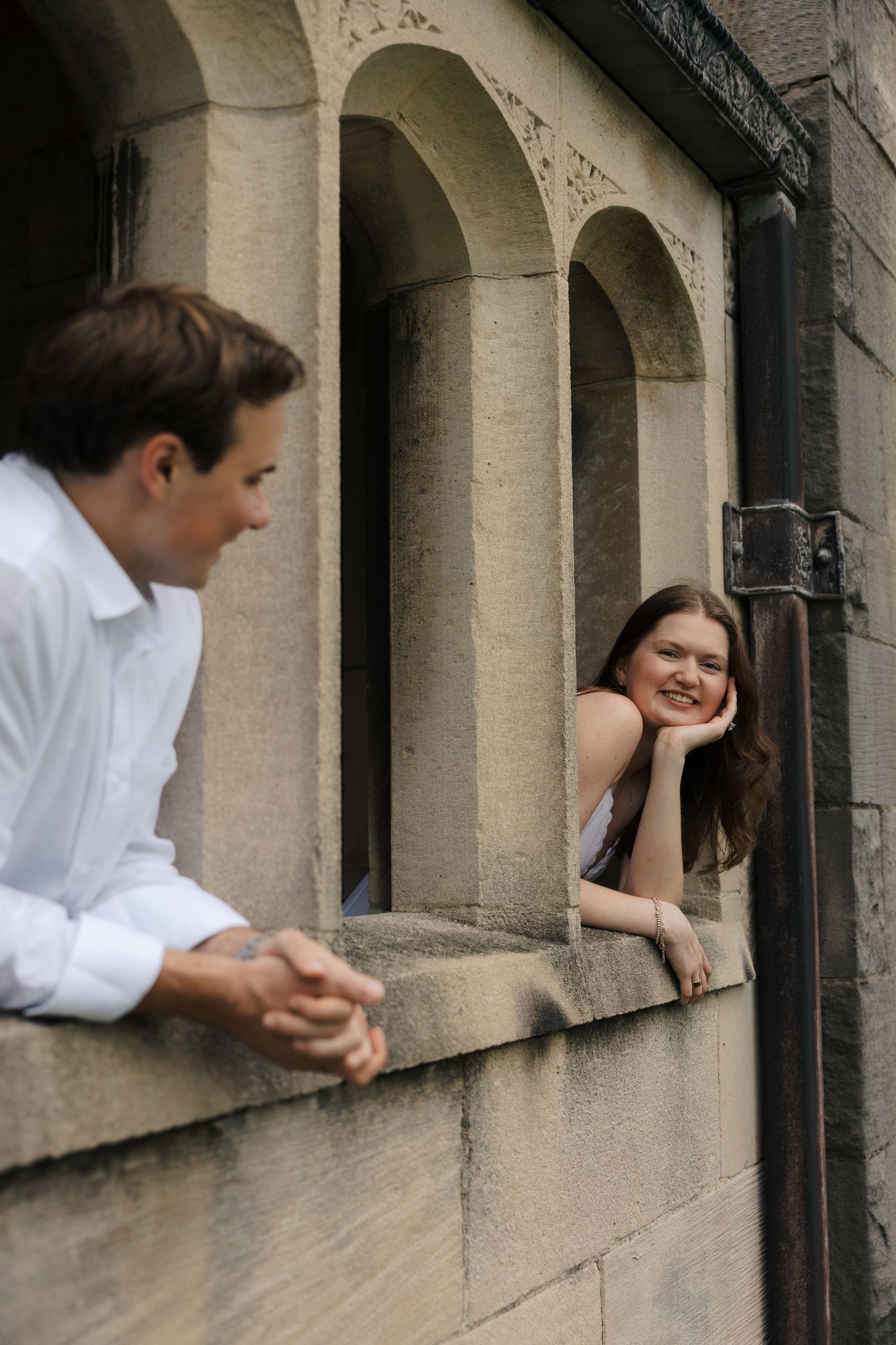 Woman leaning on a stone window ledge smiling at her partner during an engagement session.