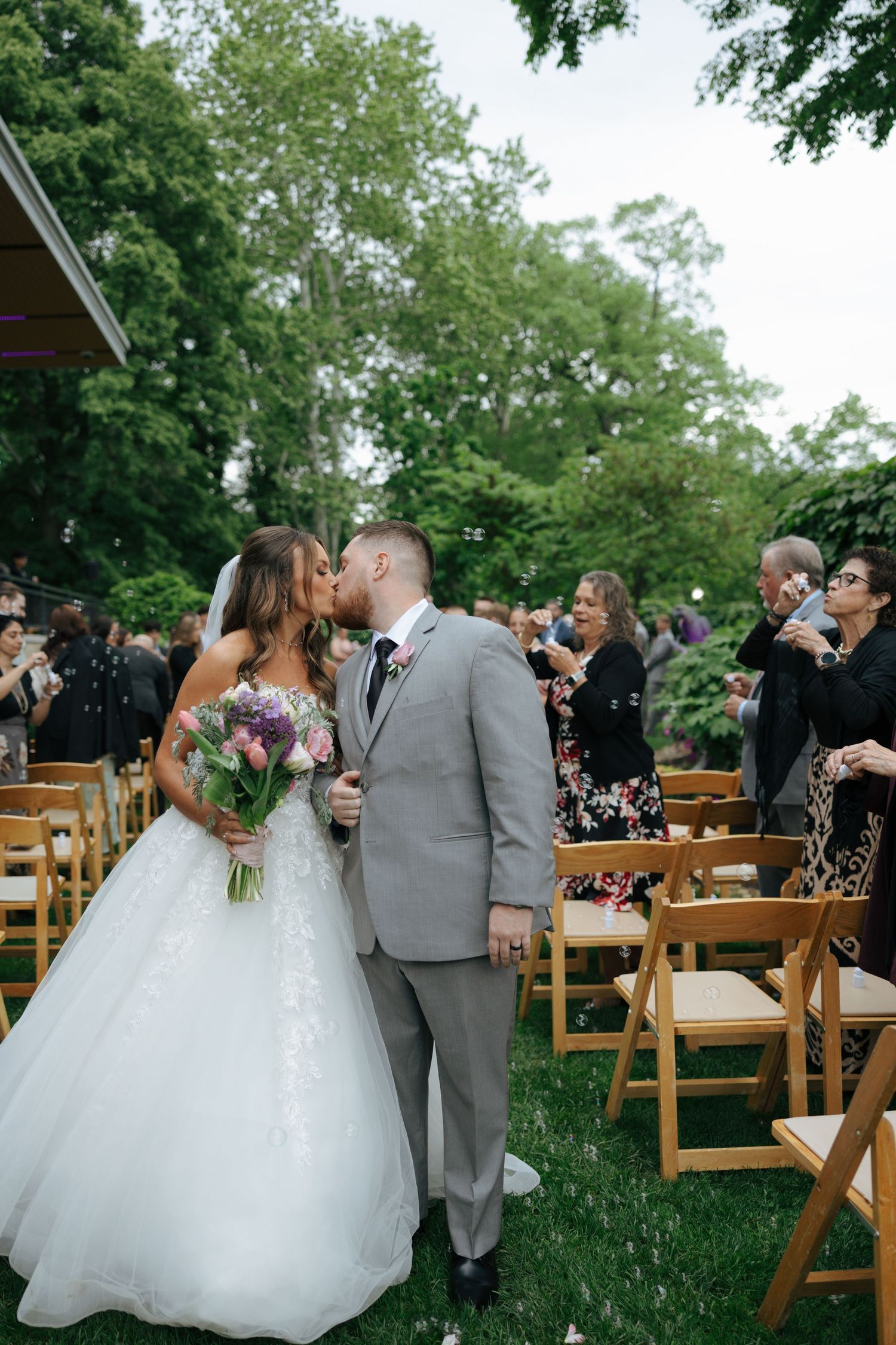 Bride and groom share first kiss as newlyweds while walking down outdoor wedding ceremony aisle.