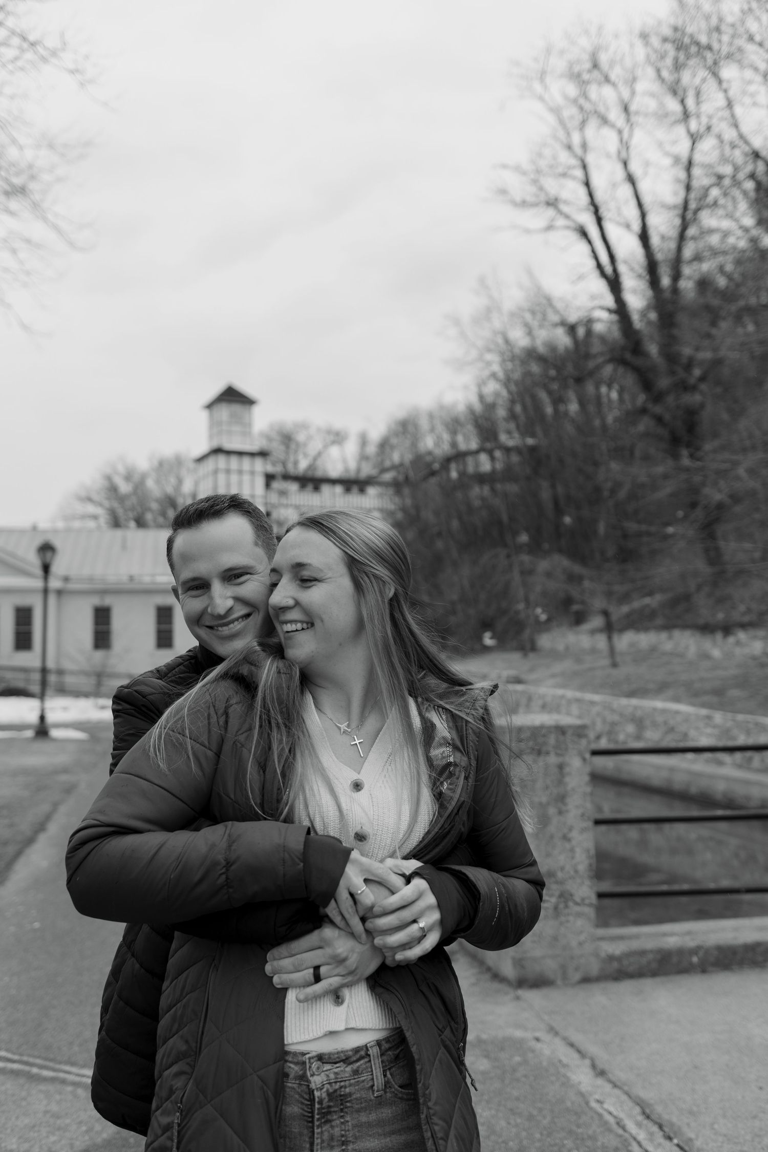 A couple shares a playful and affectionate moment together in a park on an overcast day.