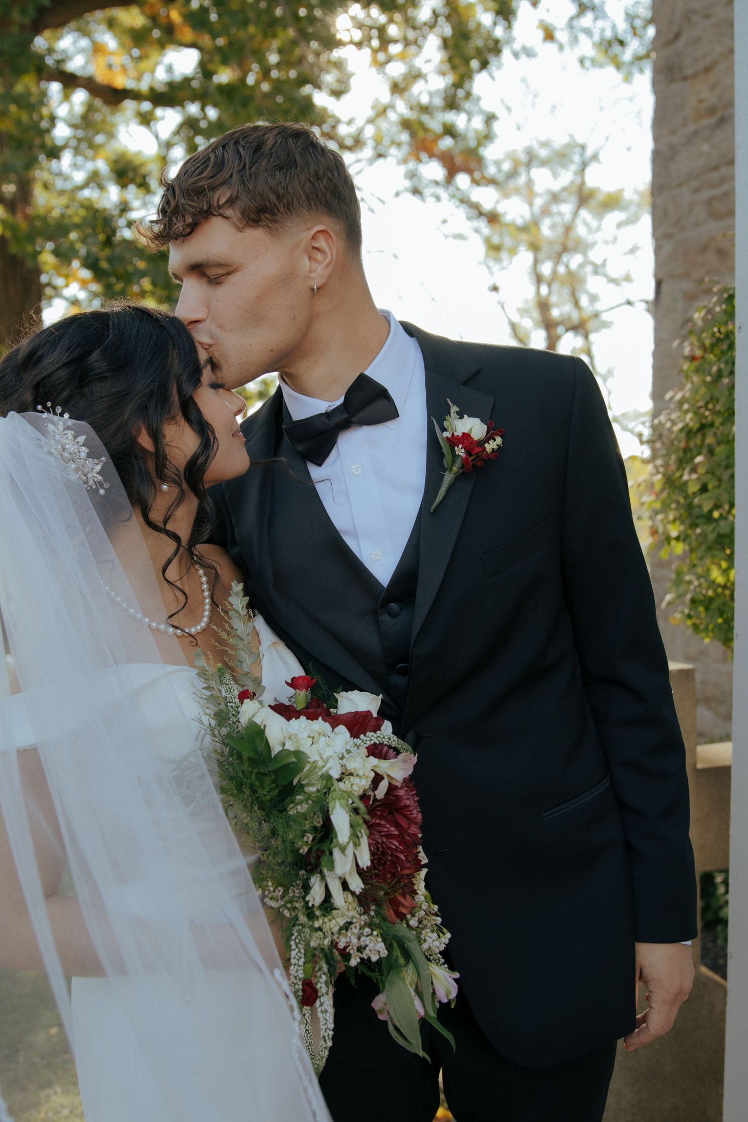 A romantic wedding couple shares three intimate kisses in a garden setting with sunlight filtering through trees.