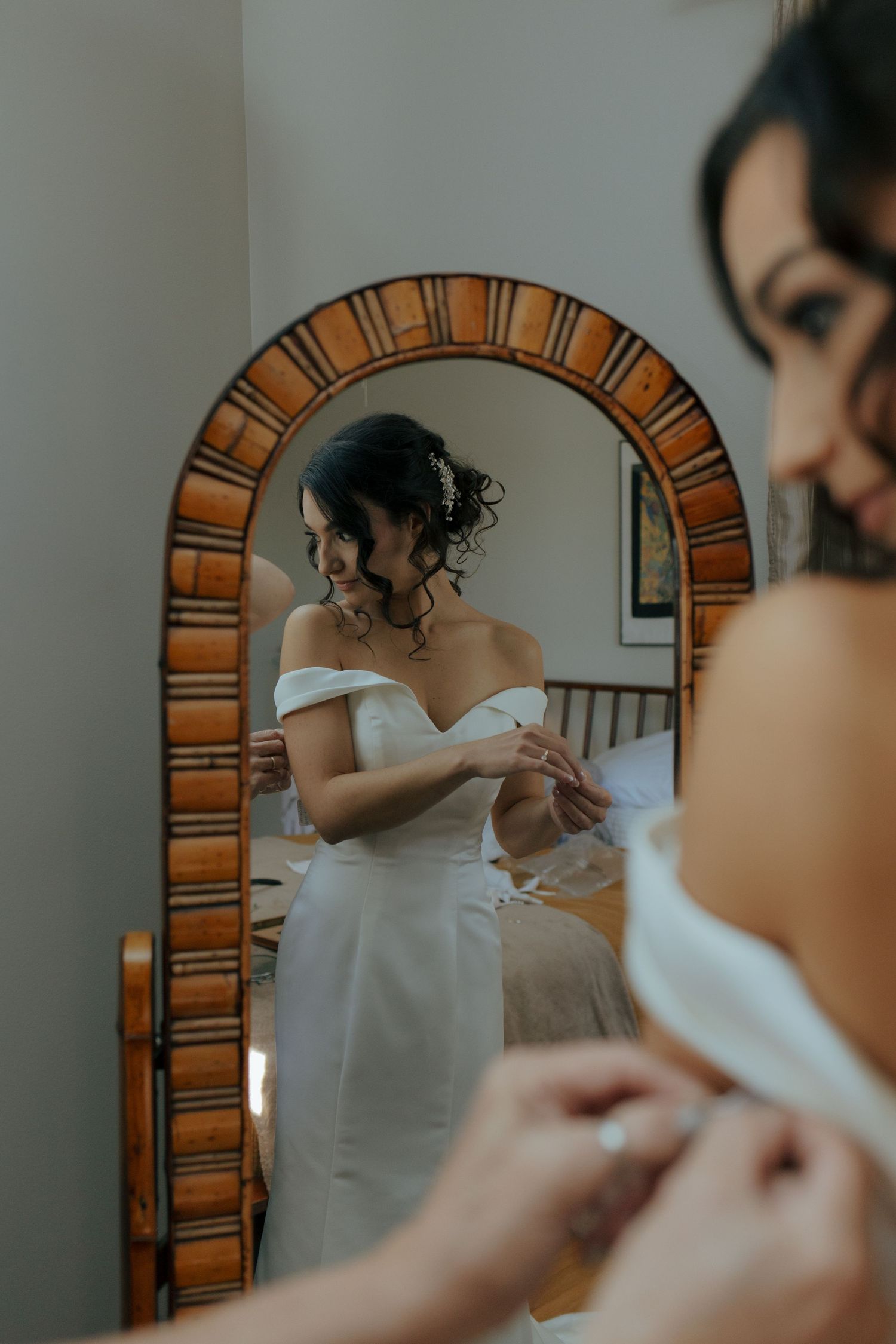 A person in a white dress adjusts their garment while getting ready in front of an arched mirror.