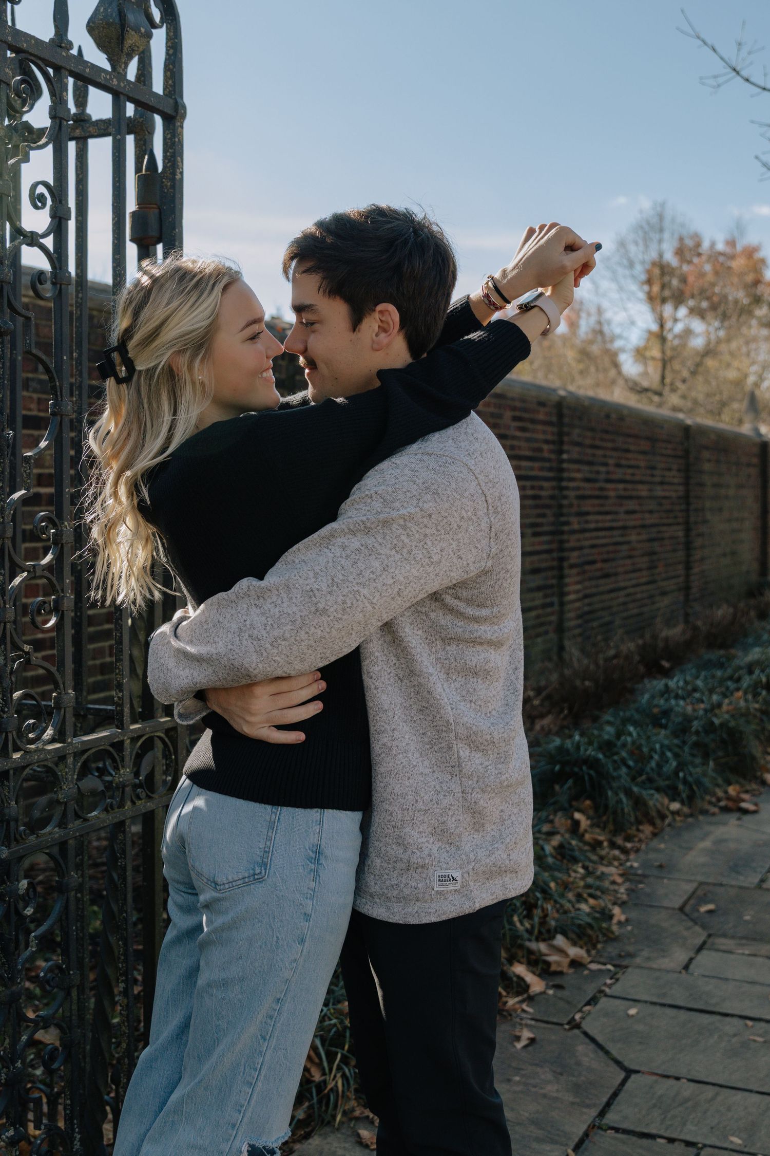 A couple embraces playfully in three candid outdoor photos against a brick wall and iron gate.
