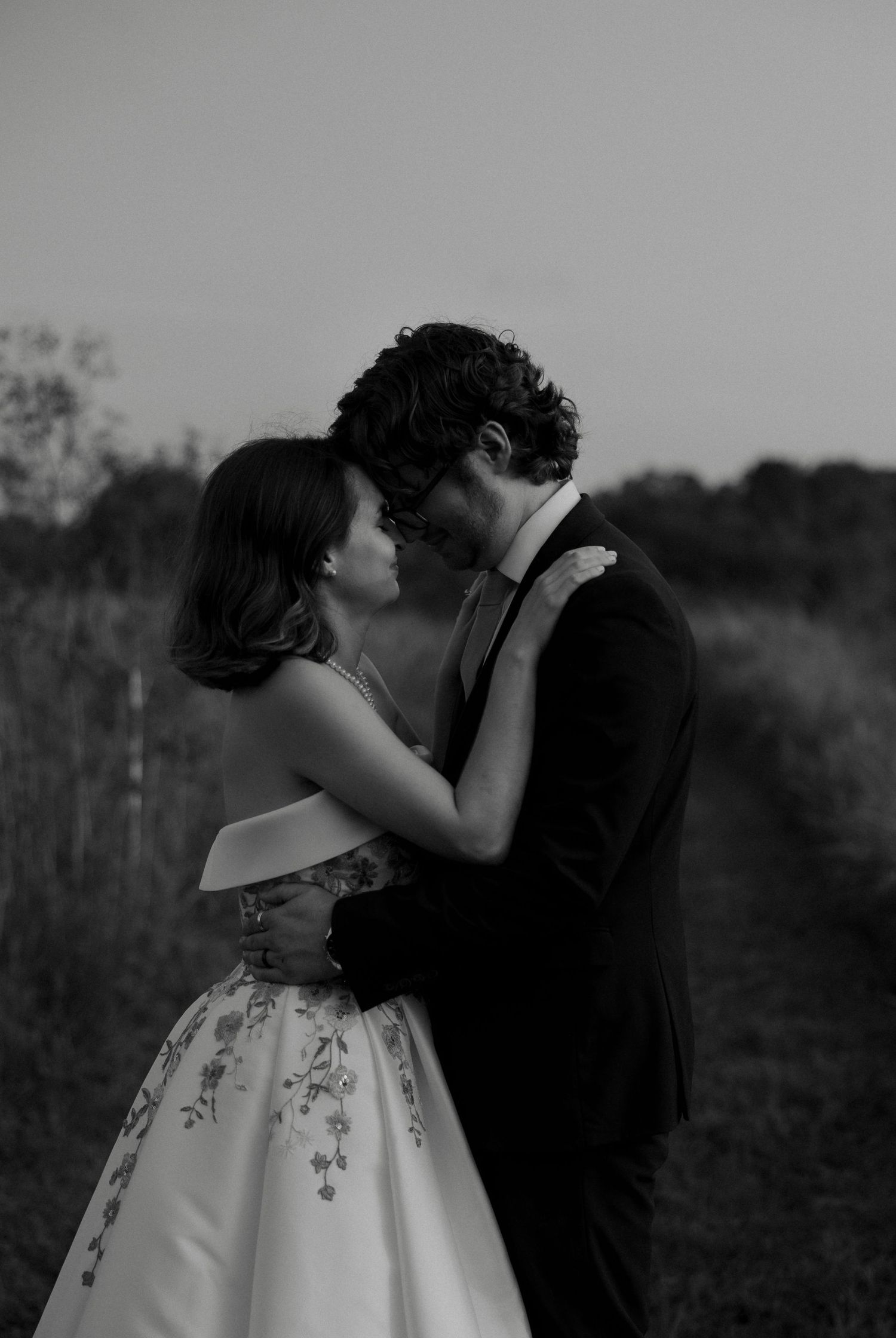 Black and white photo of bride and groom sharing a kiss in an outdoor field.