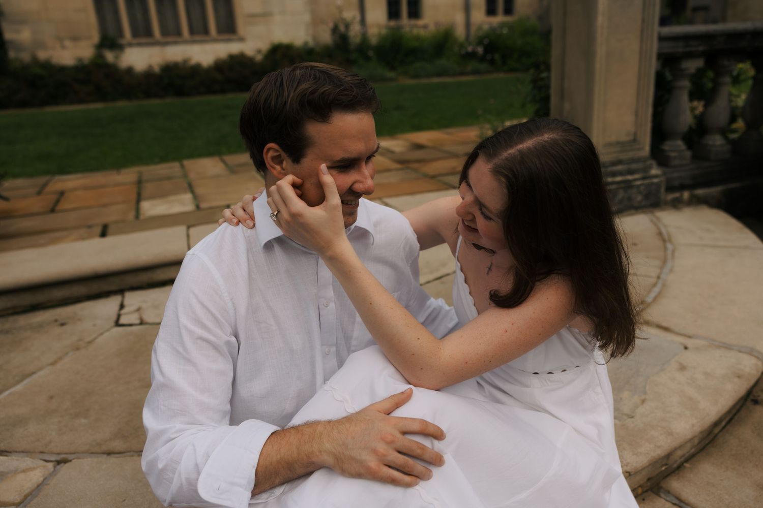 Couple sitting on stone steps, woman gently touching mans face while laughing together outdoors.