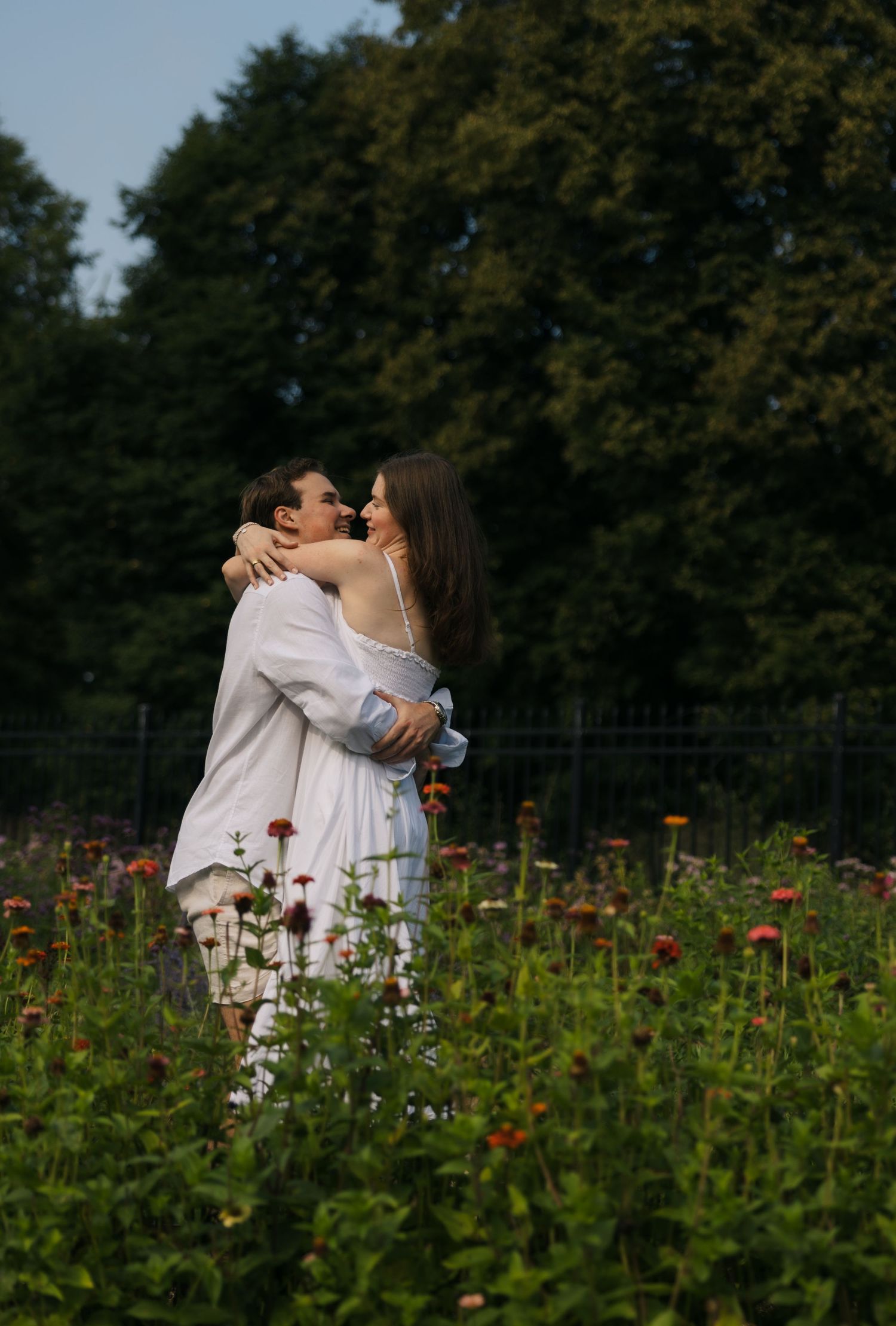 Couple sharing a tender hug surrounded by vibrant blooming flowers in lush garden on a sunny day.