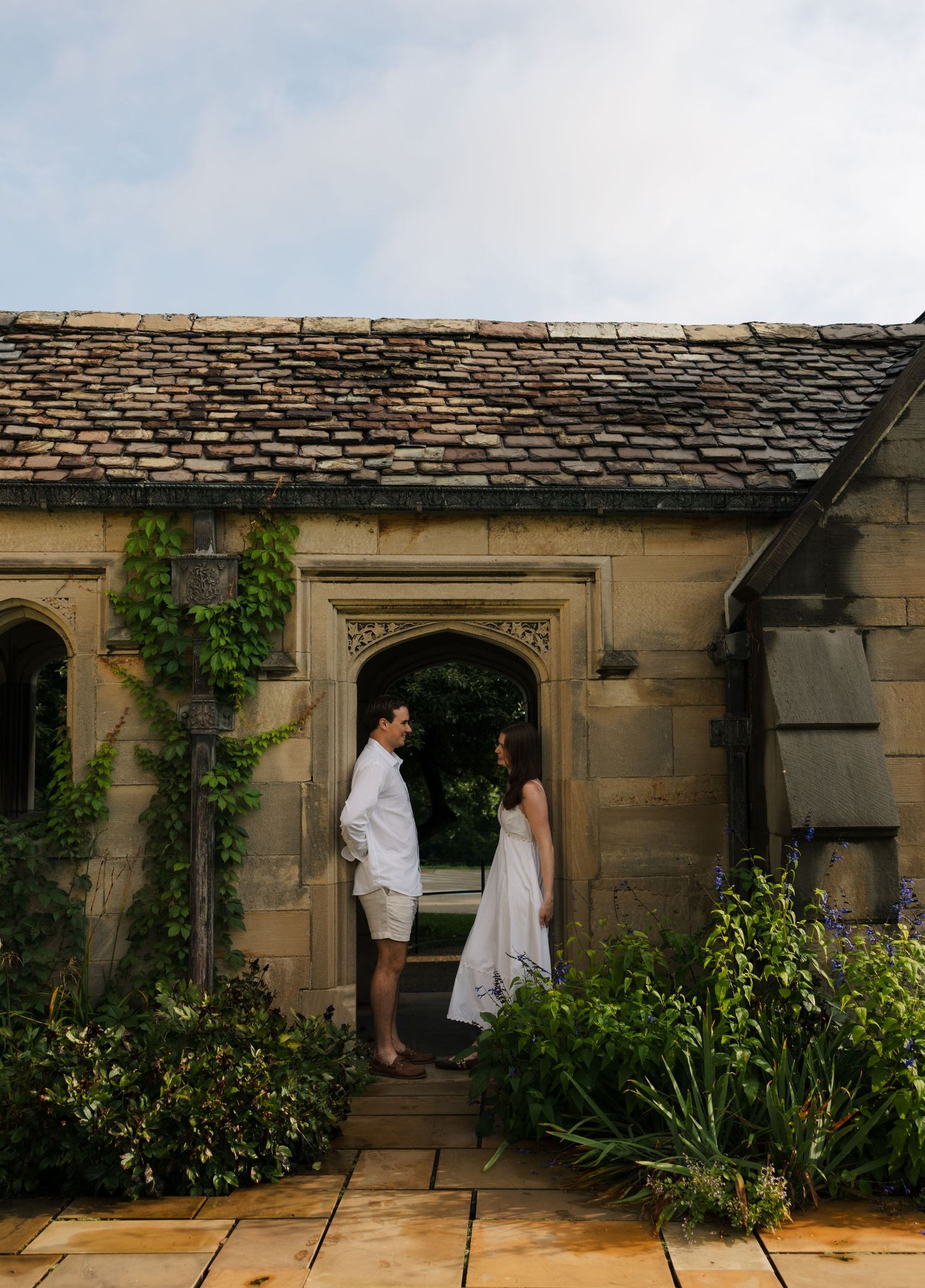 A couple stands facing each other in an arched stone doorway surrounded by lush ivy at a historic estate.