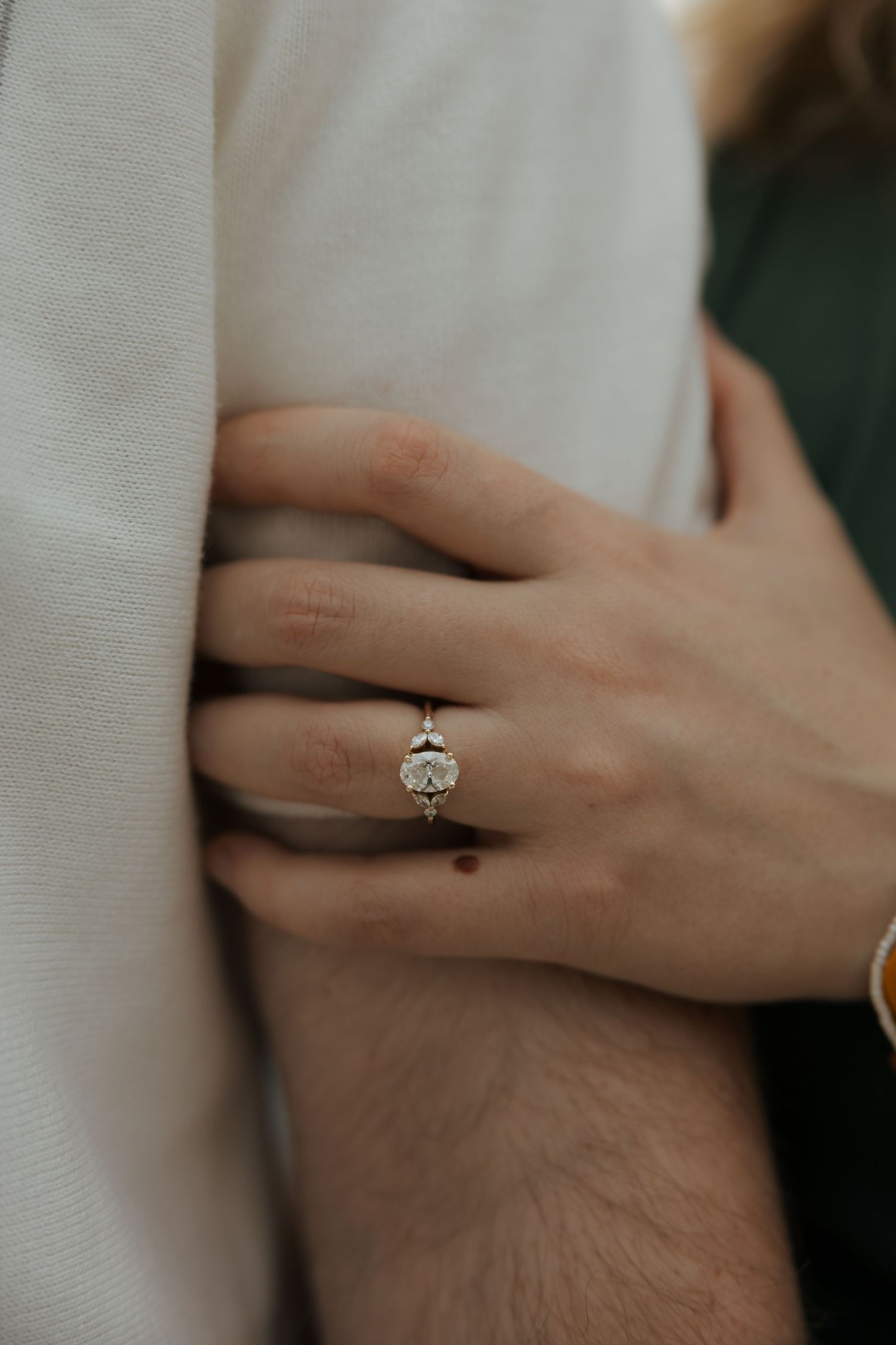 Close-up of a diamond halo engagement ring on a woman's finger as she embraces her partner.