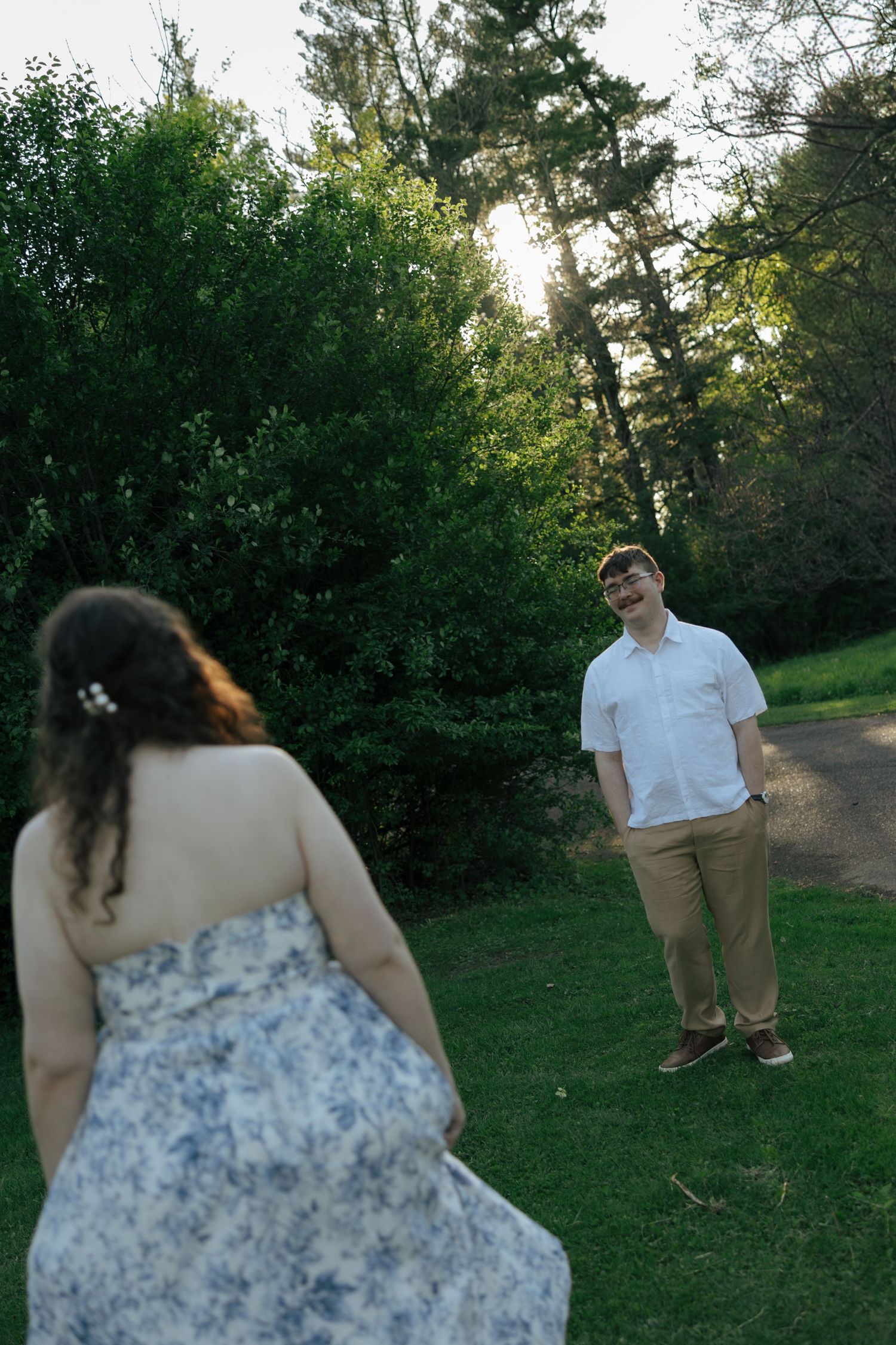 Man in white shirt smiling at woman in floral dress in a sunlit green park.