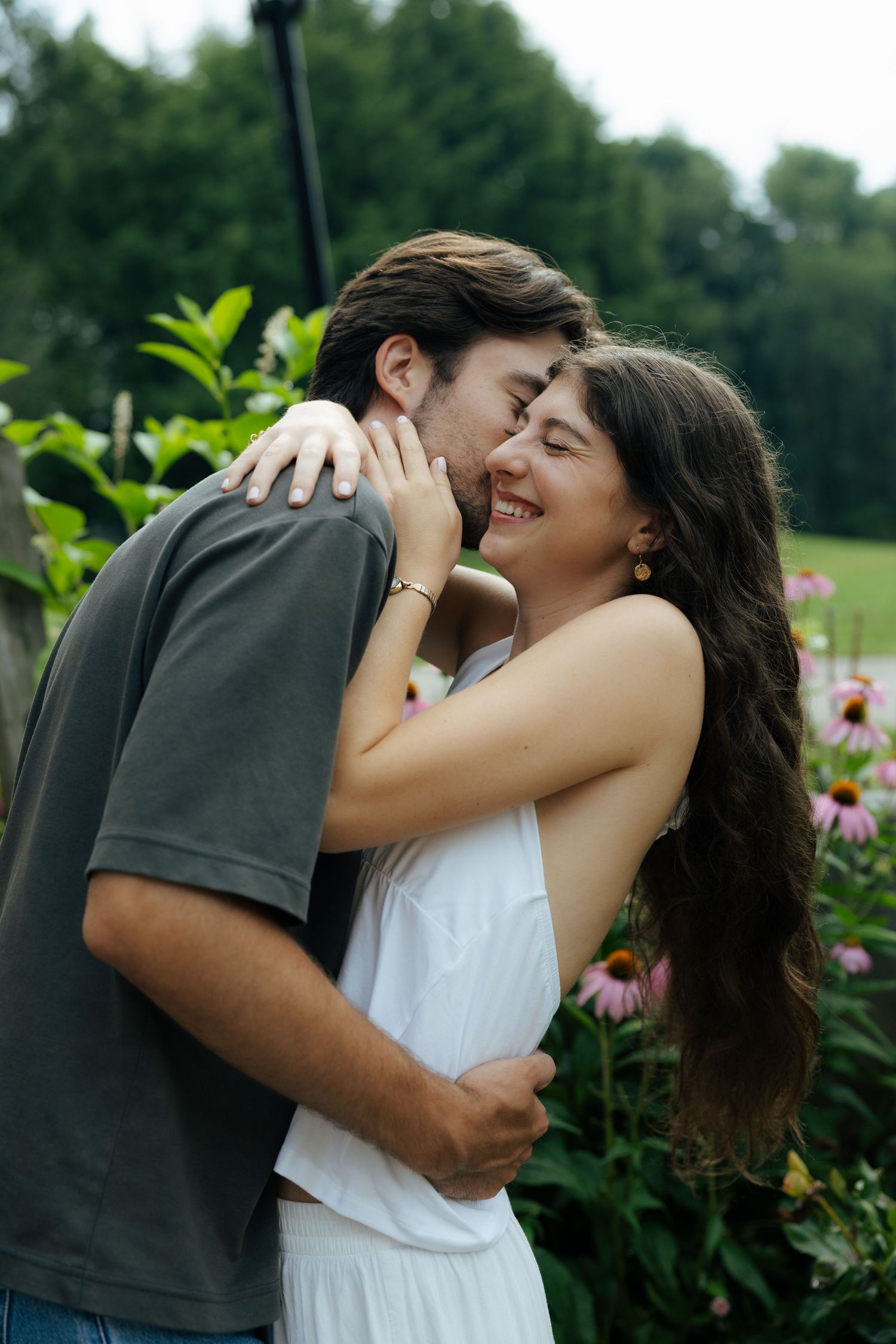A couple shares a tender embrace and kiss among blooming flowers in a garden.