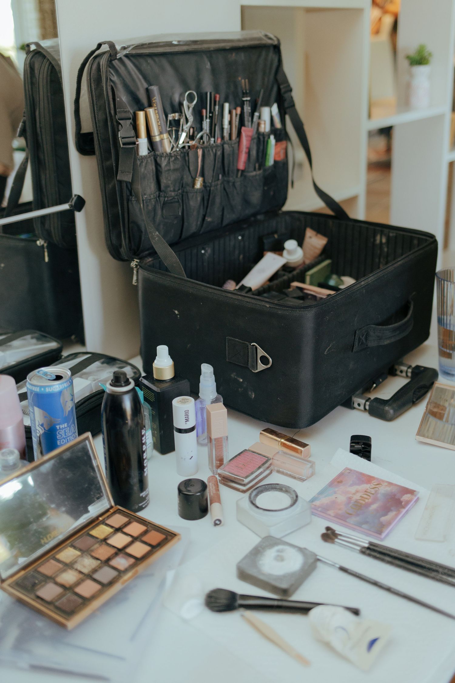 Professional makeup artist black case open on white table surrounded by cosmetics, brushes, and beauty tools.