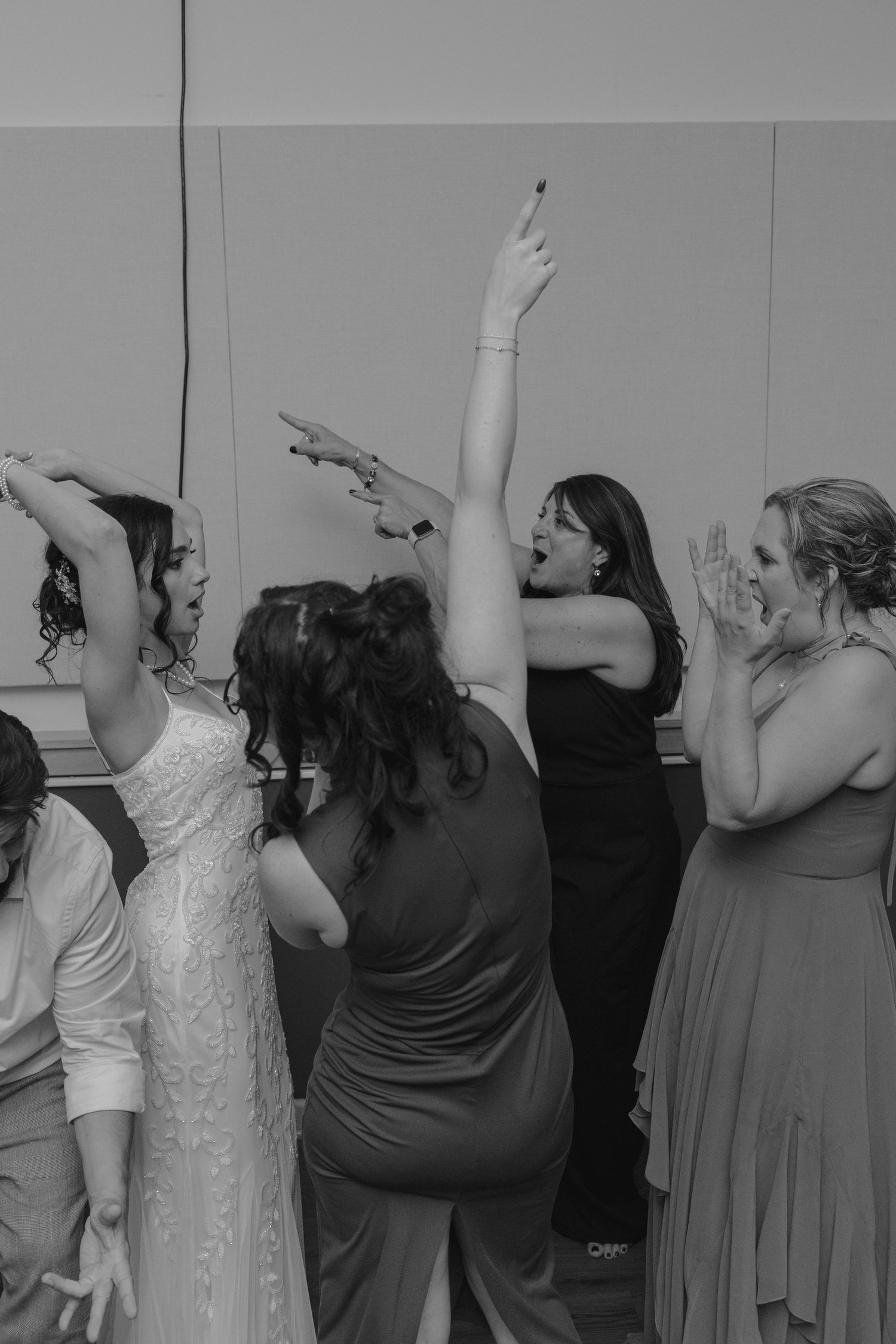 Bride and bridesmaids dancing energetically at wedding reception in black and white photo.