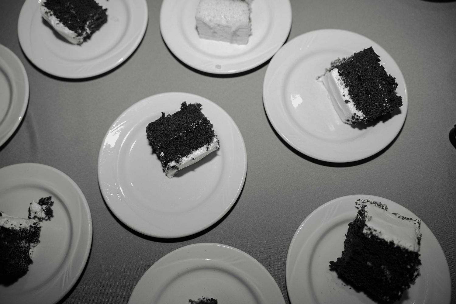 Black and white photo of chocolate cake slices with white frosting served on round white plates at a wedding reception.