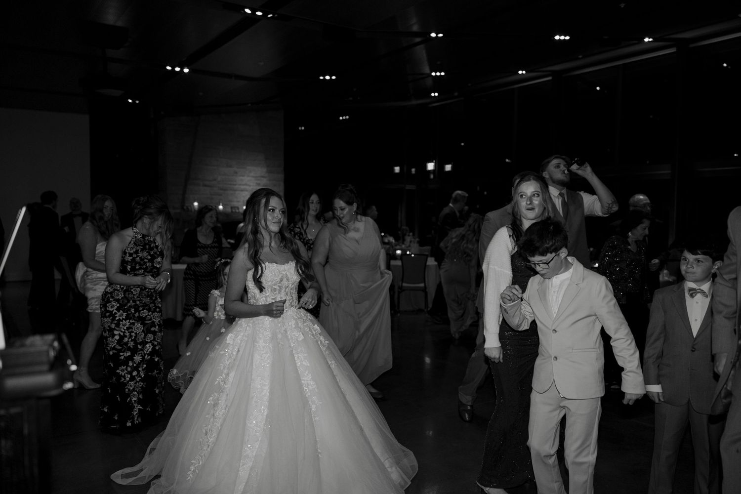 Bride in a white ball gown dances with a young boy in a suit at a wedding reception.
